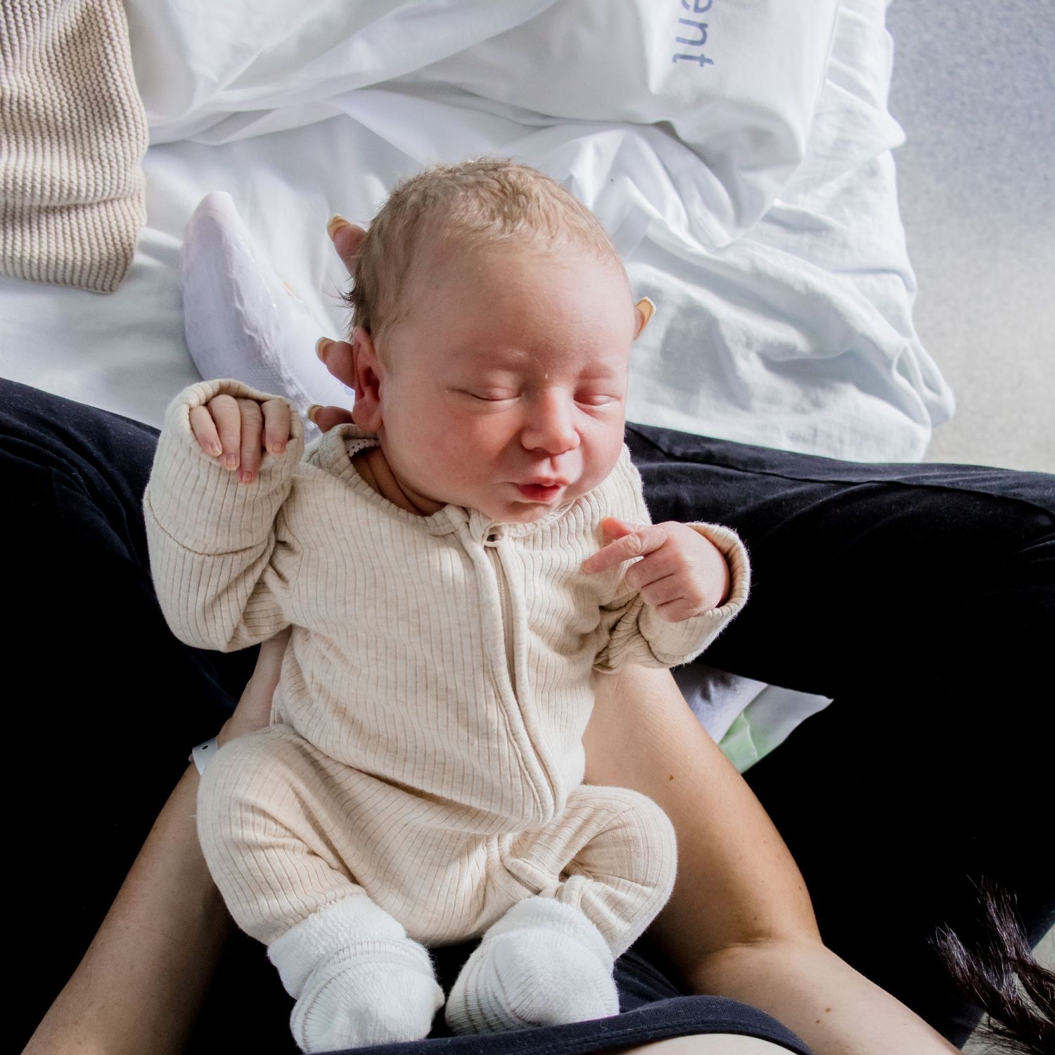 Sleepy newborn in cream zippered onesie stretches while lying down.
