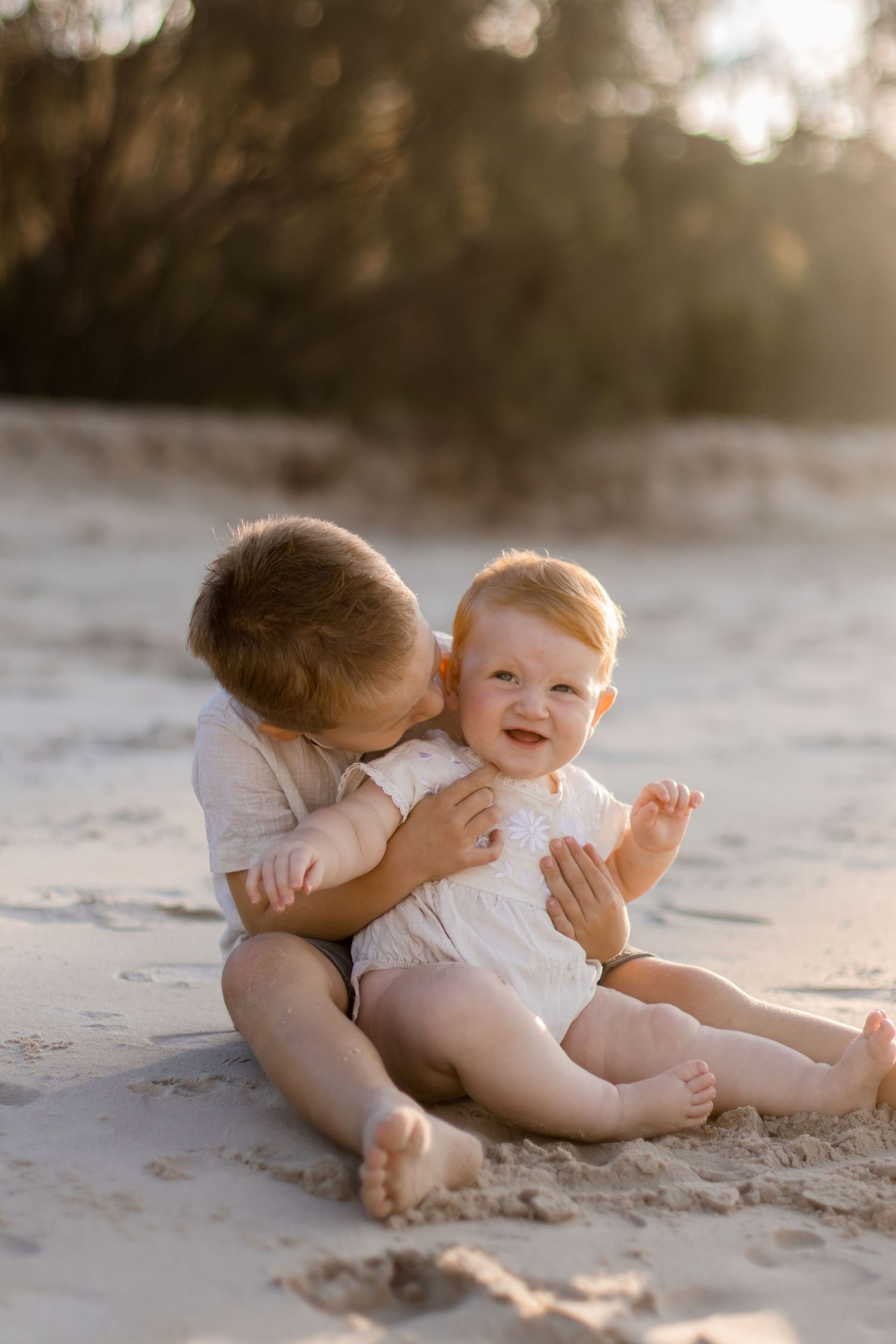 Two young siblings share sweet moments playing together in the sand at sunset.