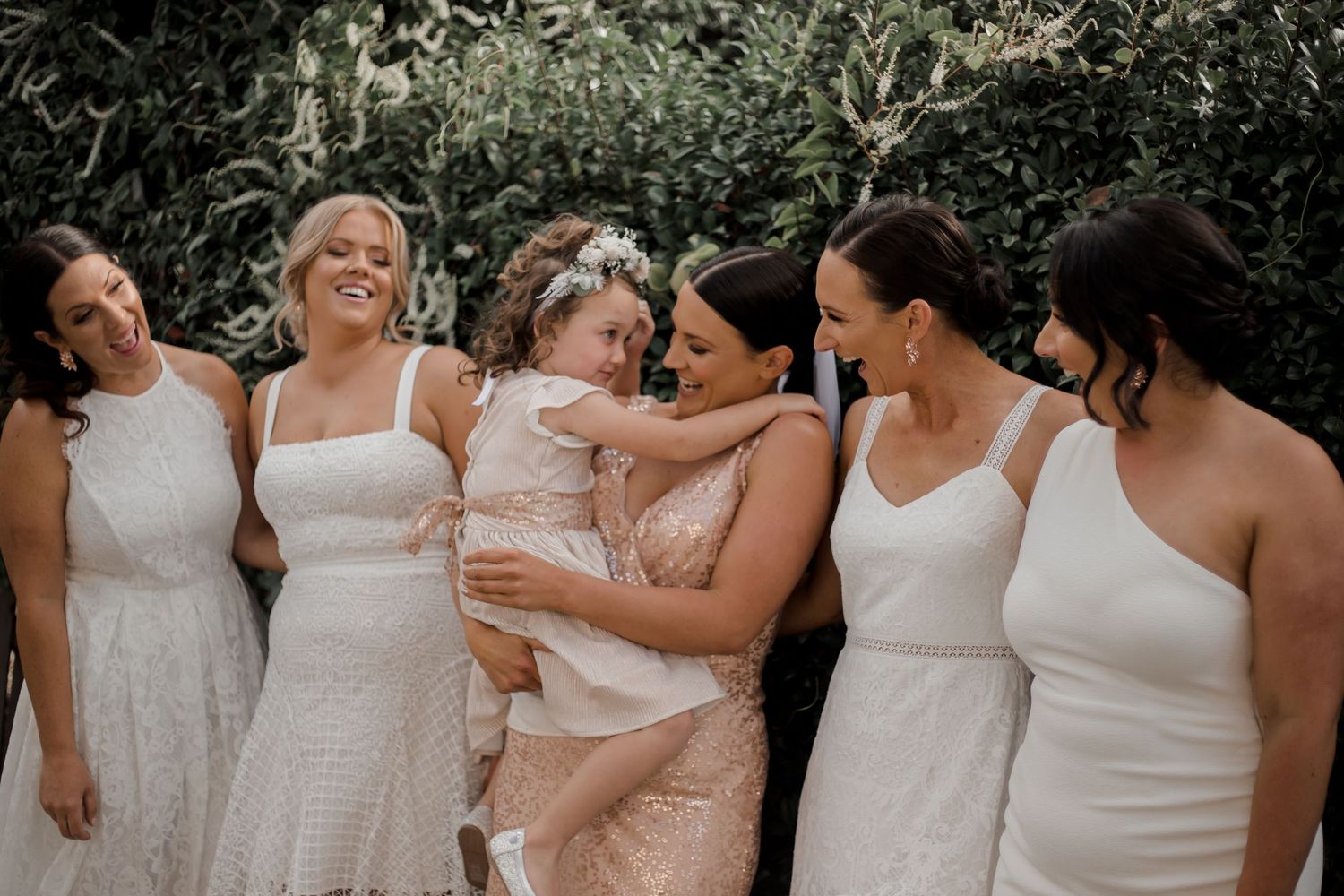 A group of bridesmaids wearing white dresses gather together for a candid photo during wedding celebrations.