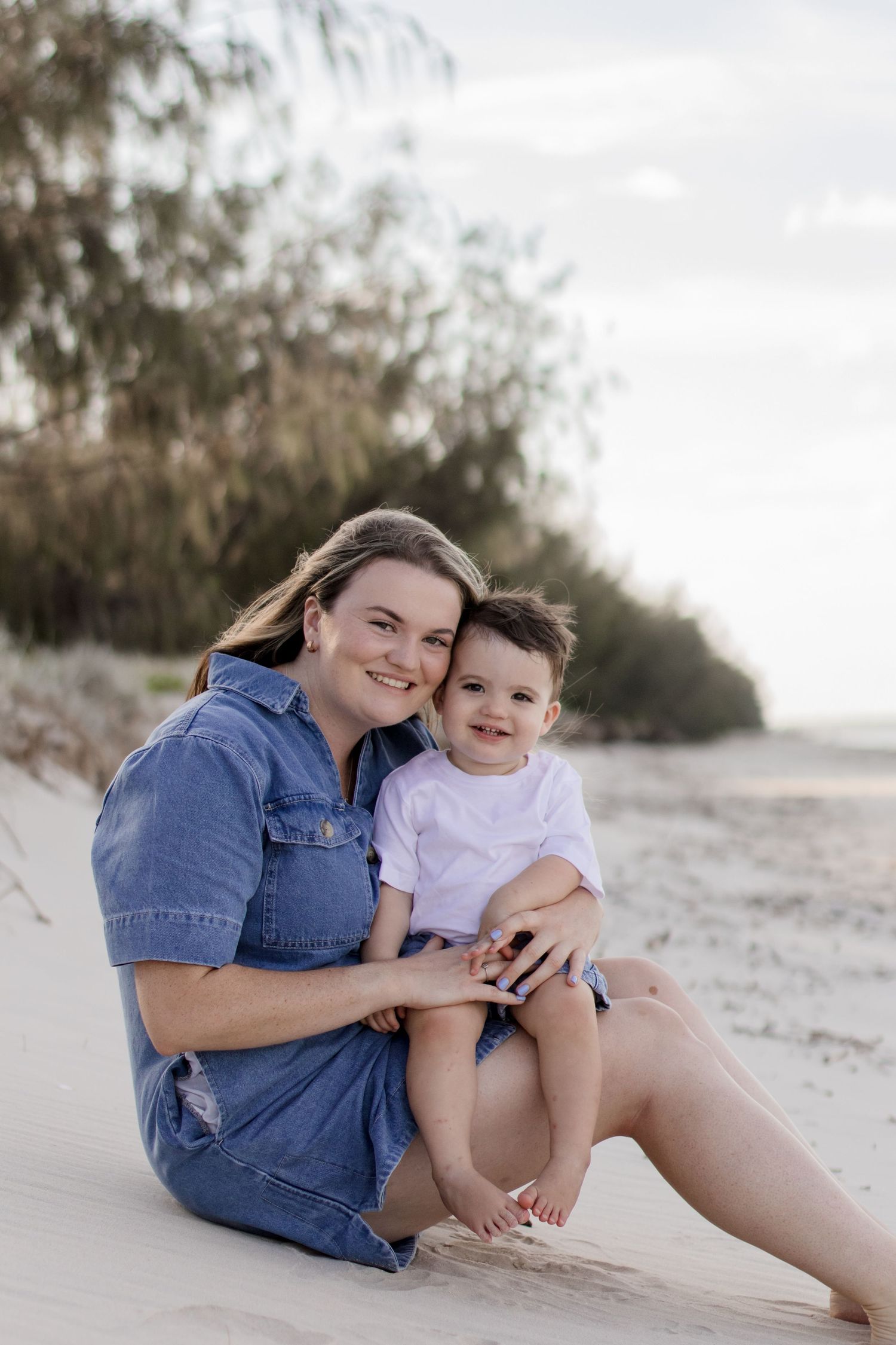Casual beach portrait of two people sitting in the sand wearing denim and white clothing.