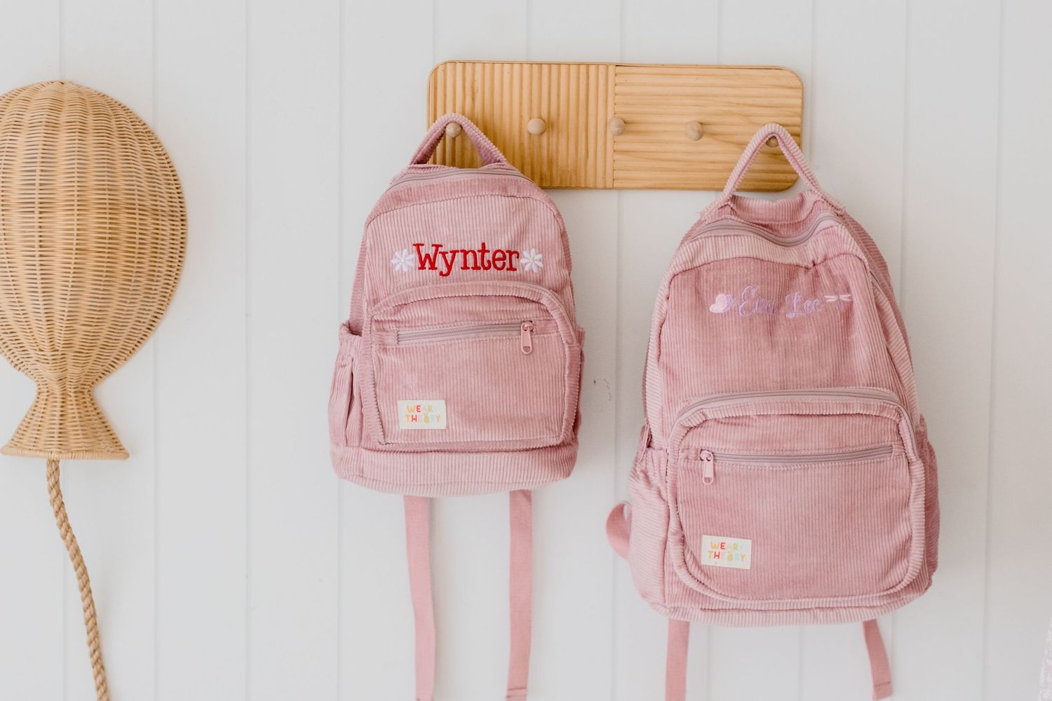 Pink vintage backpacks and lanterns arranged in a row against a white textured wall for aesthetic decor.