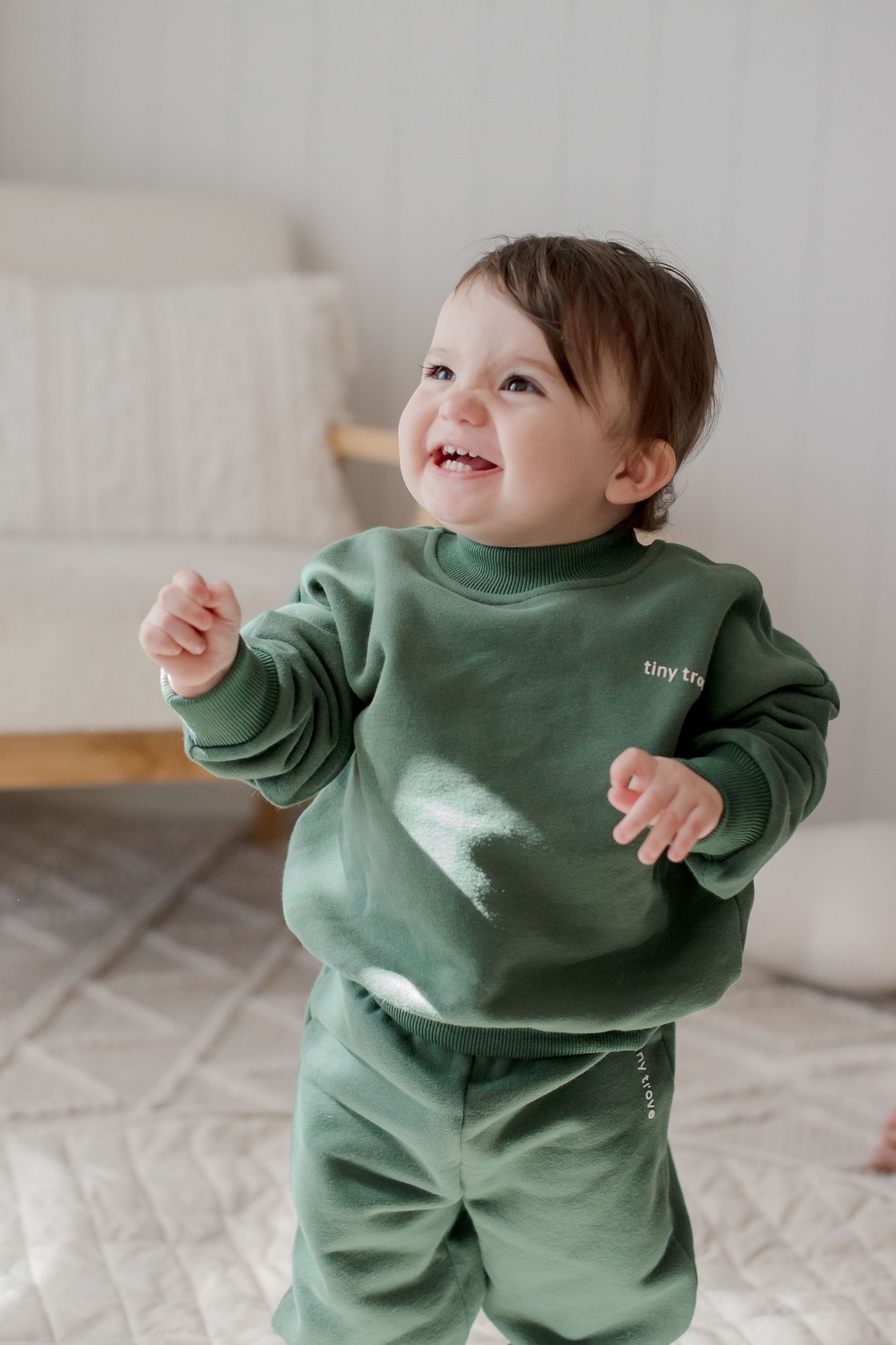 Toddler wearing cozy sage green sweatsuit smiling and playing indoors.