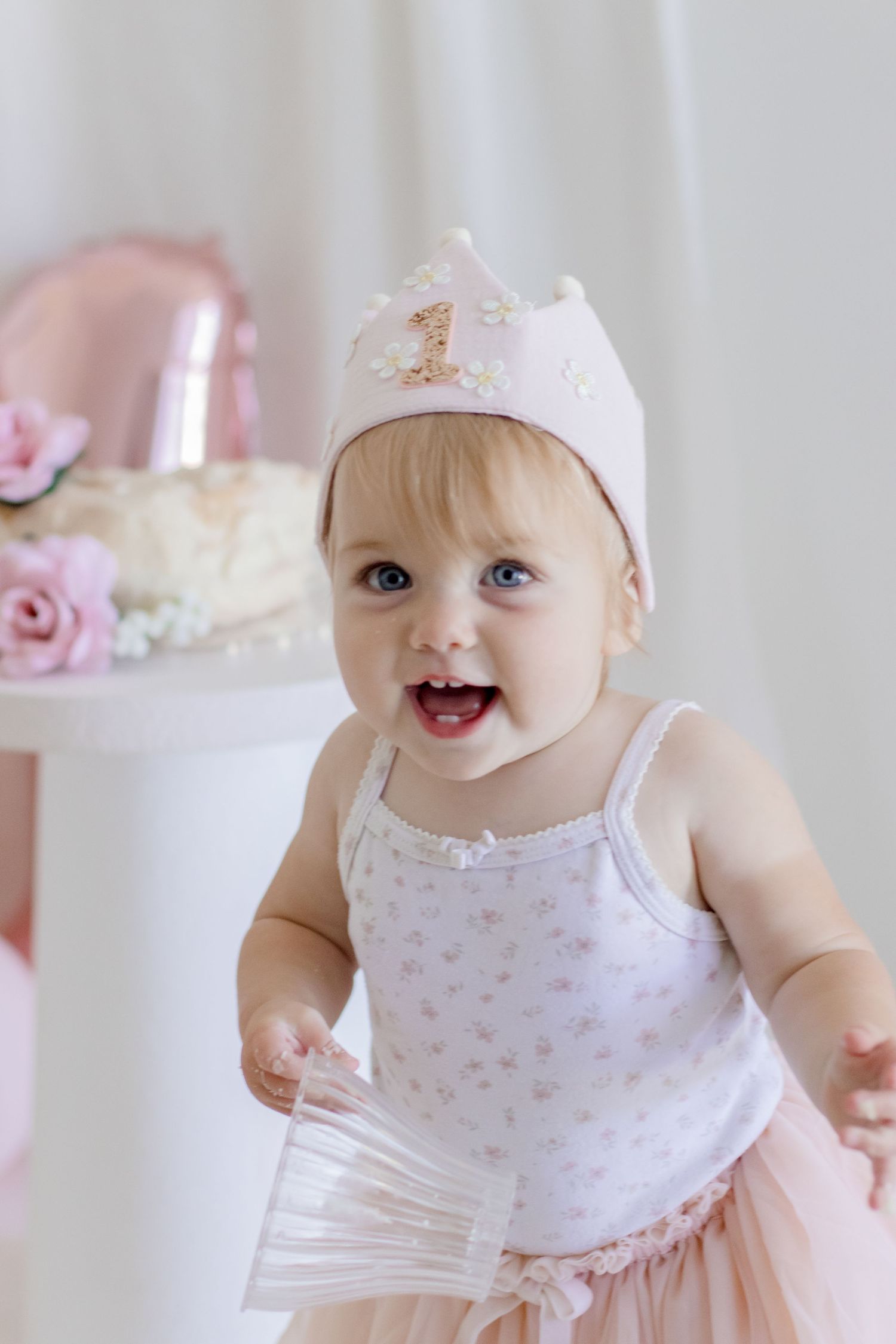 A happy toddler in tulle dress and crown poses with pink party decorations.