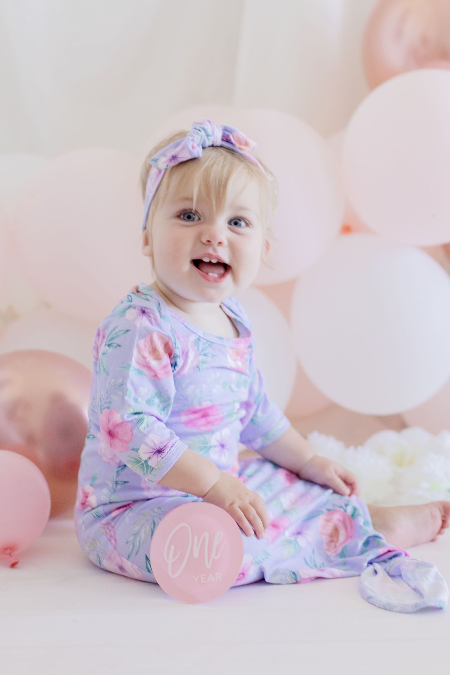 Happy infant wearing floral sleepwear poses with pink and white balloons.