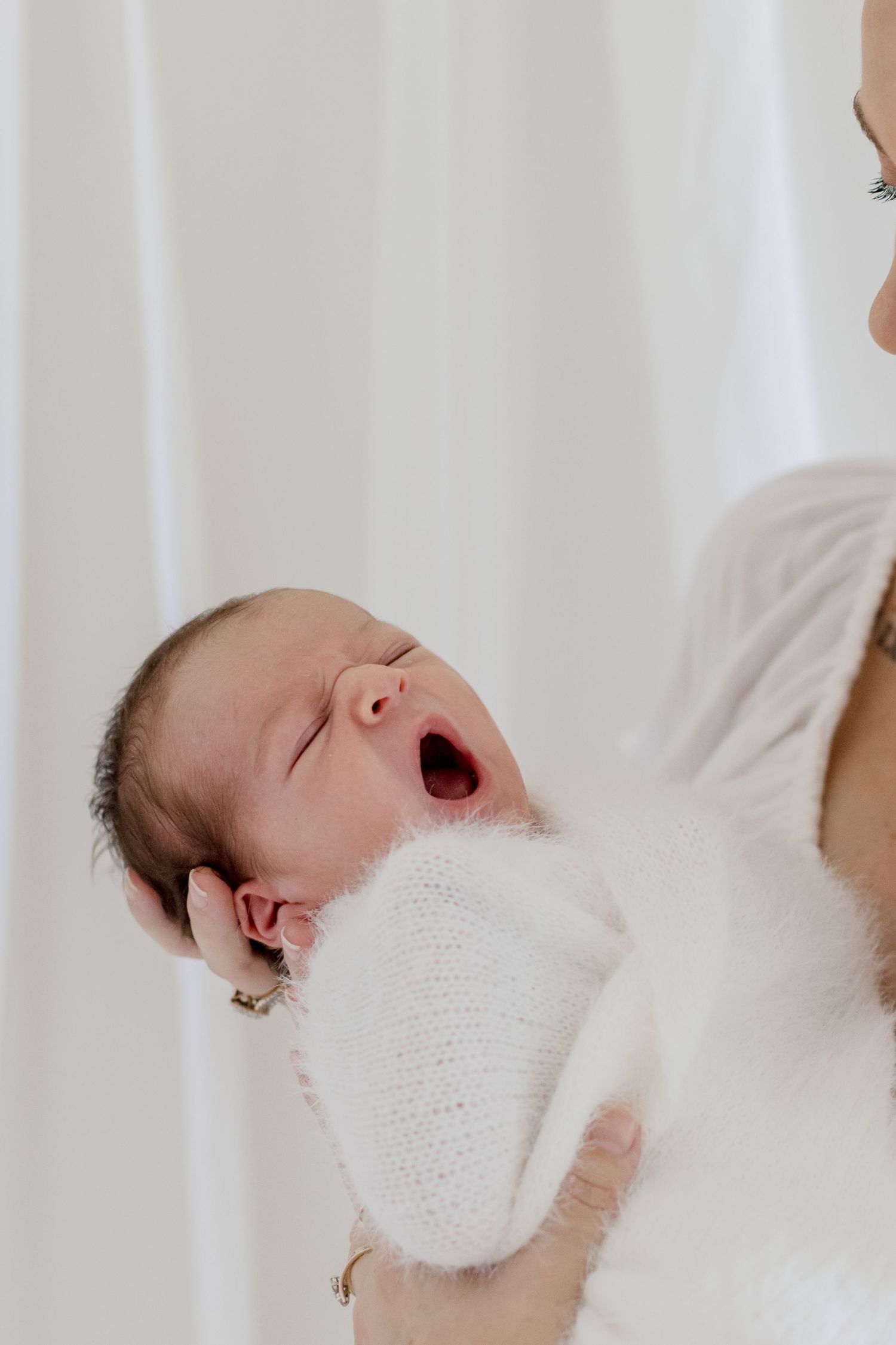 Newborn baby yawning while wrapped in cozy white knit blanket.