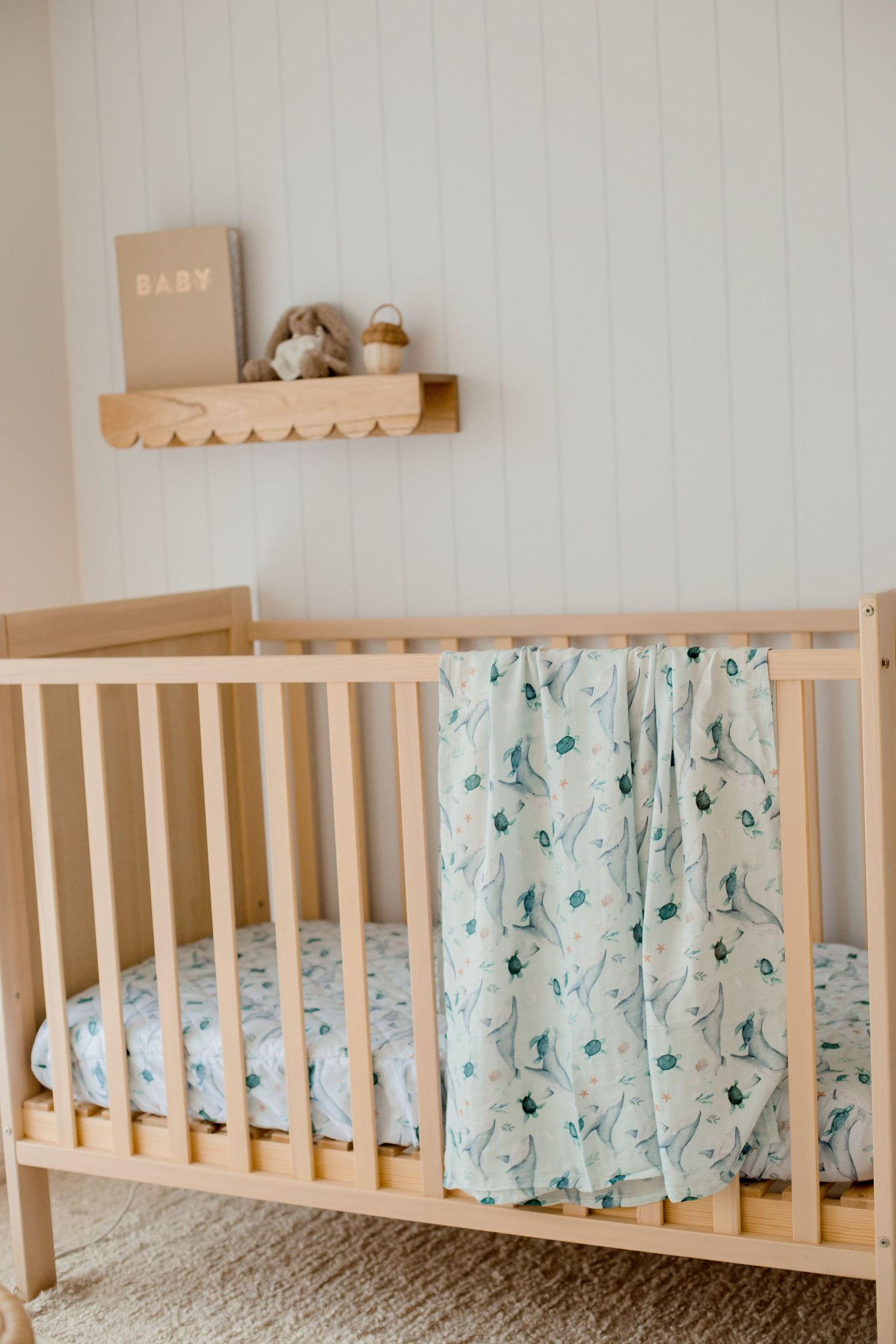 Modern nursery with white crib, mint floral bedding, and wooden shelf adorned with baby items.