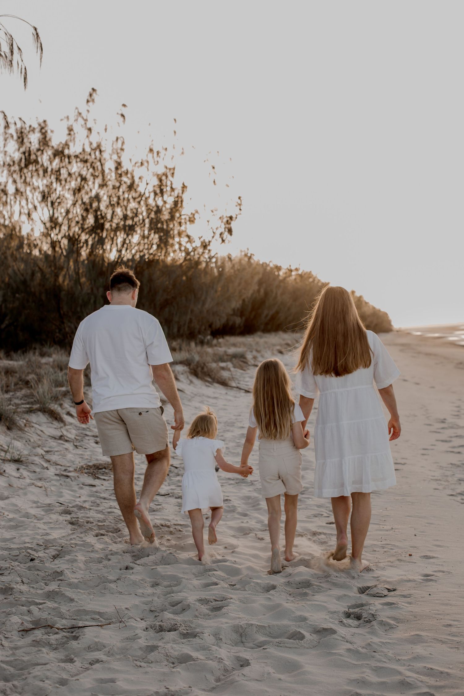 Family walking together on sandy beach at sunset holding hands.