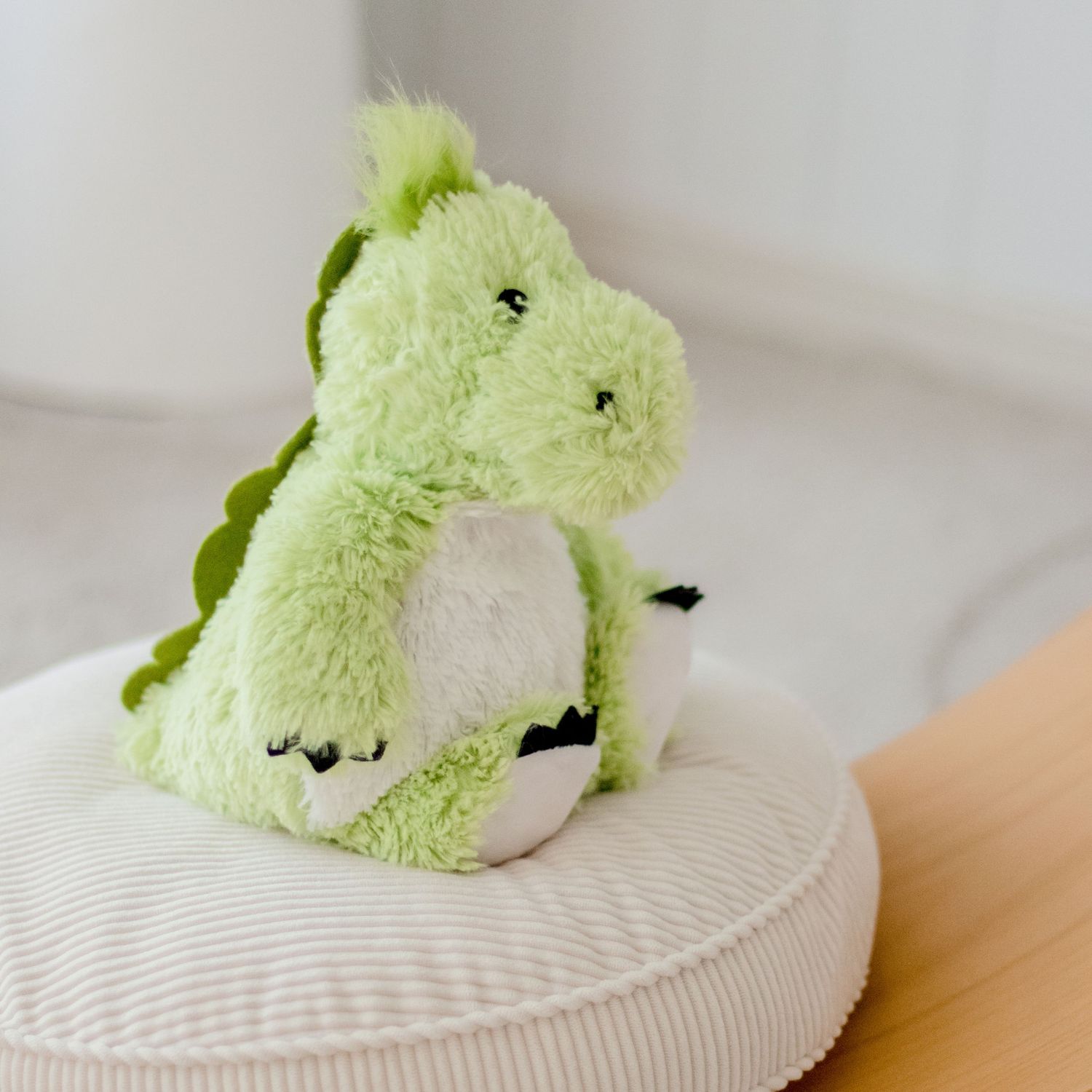 Cute plush green dinosaur stuffed animal sitting on white cushion.