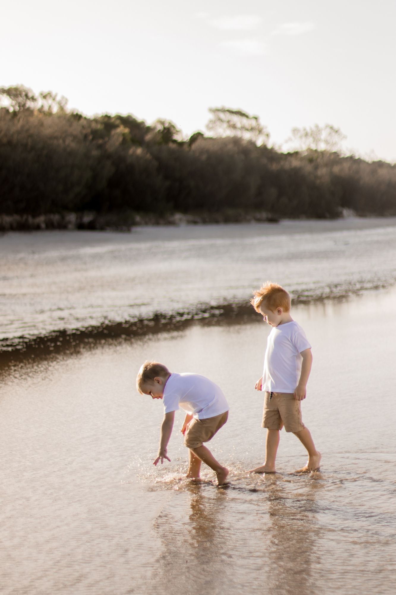 Two children playing and splashing in shallow water at sunset on a peaceful beach.