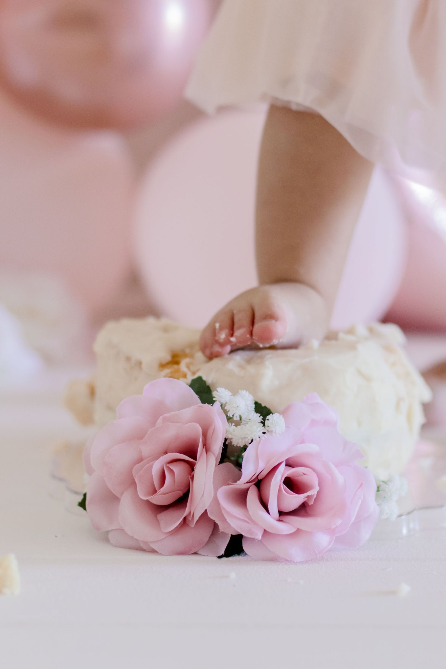 Tiny hand touching pink roses amidst cream-colored party decorations.