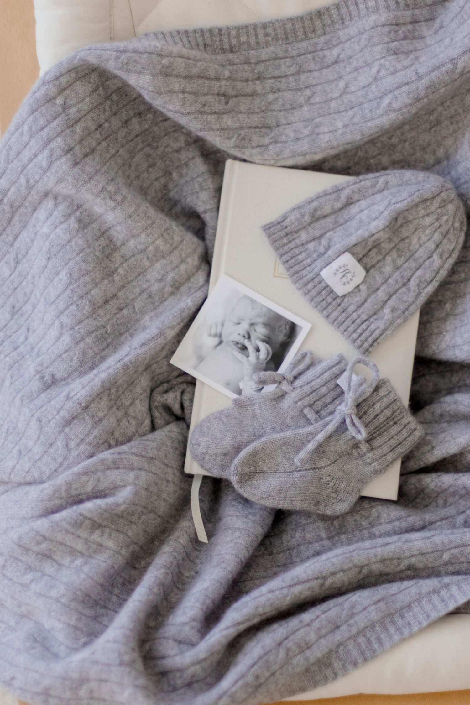 Gray knit baby accessories including a sweater, hat and booties arranged with a vintage photograph.