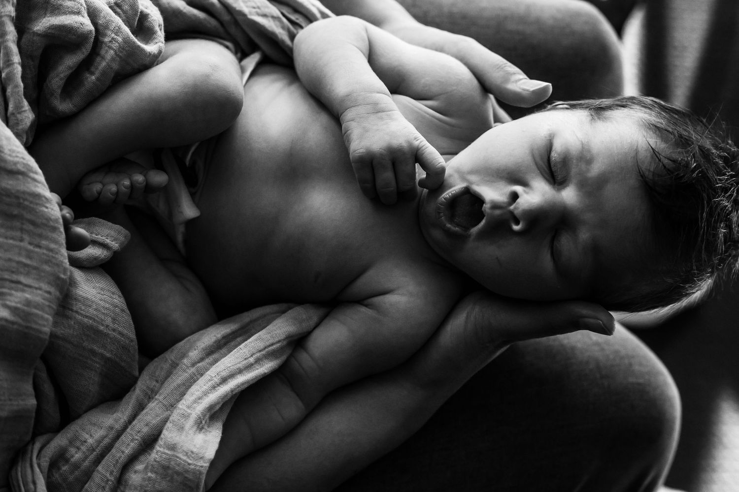 A newborn baby rests peacefully against someone's chest in an intimate black and white photograph.