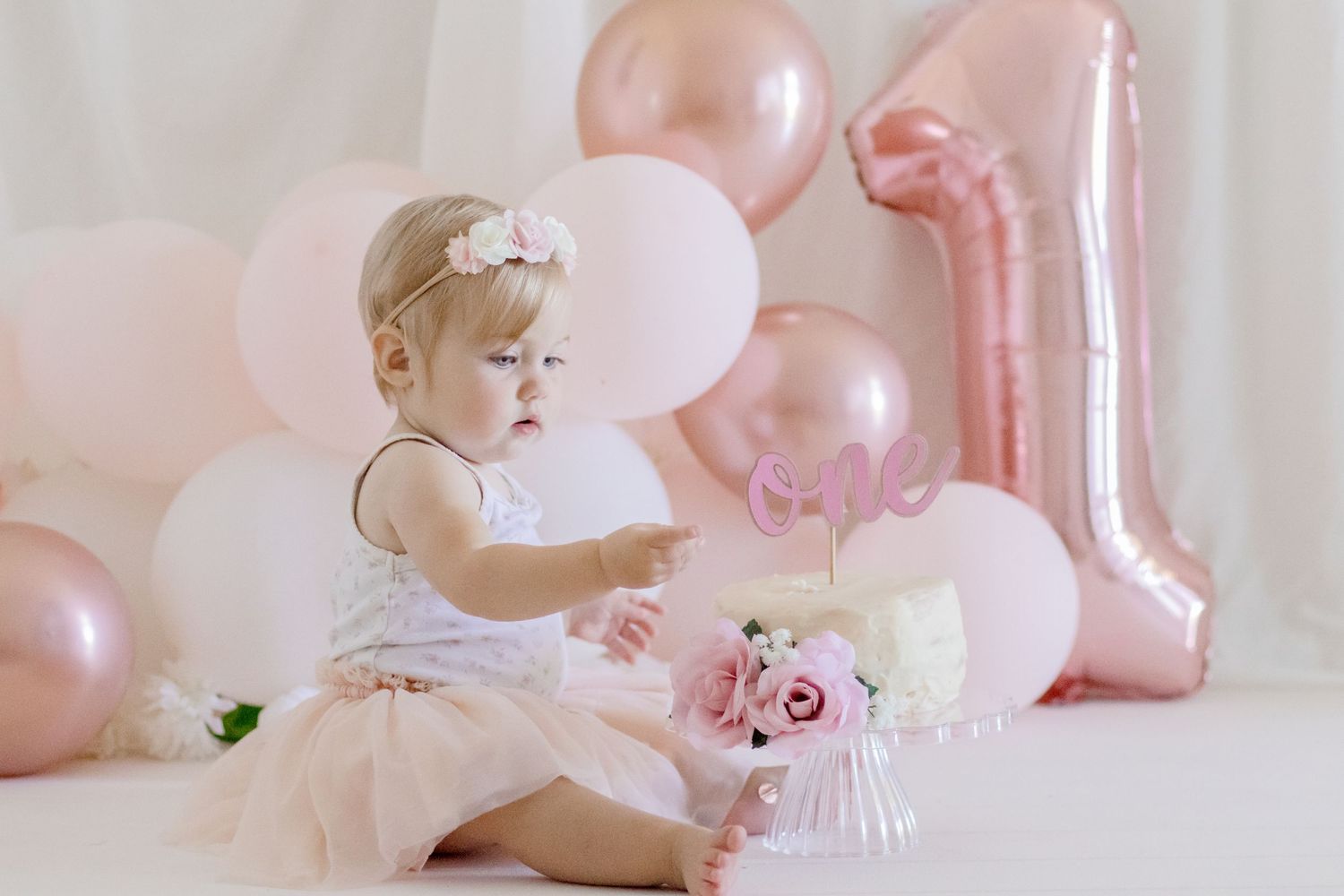 Child in tutu exploring first birthday decorations with pink balloons.