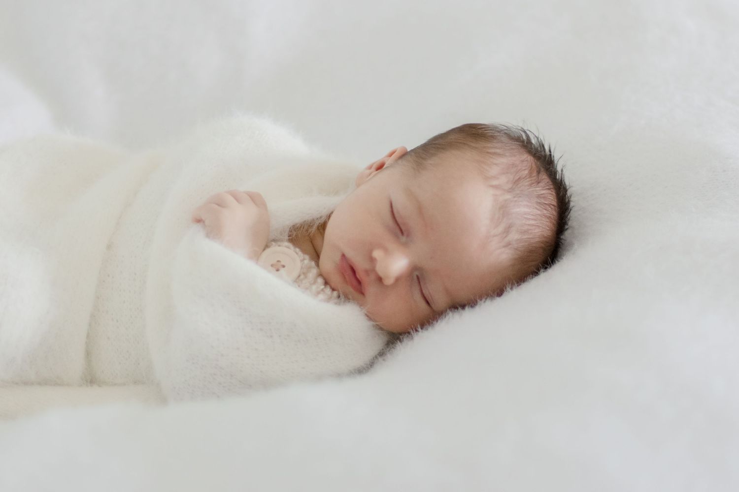 Serene newborn baby sleeping soundly in soft white swaddle.