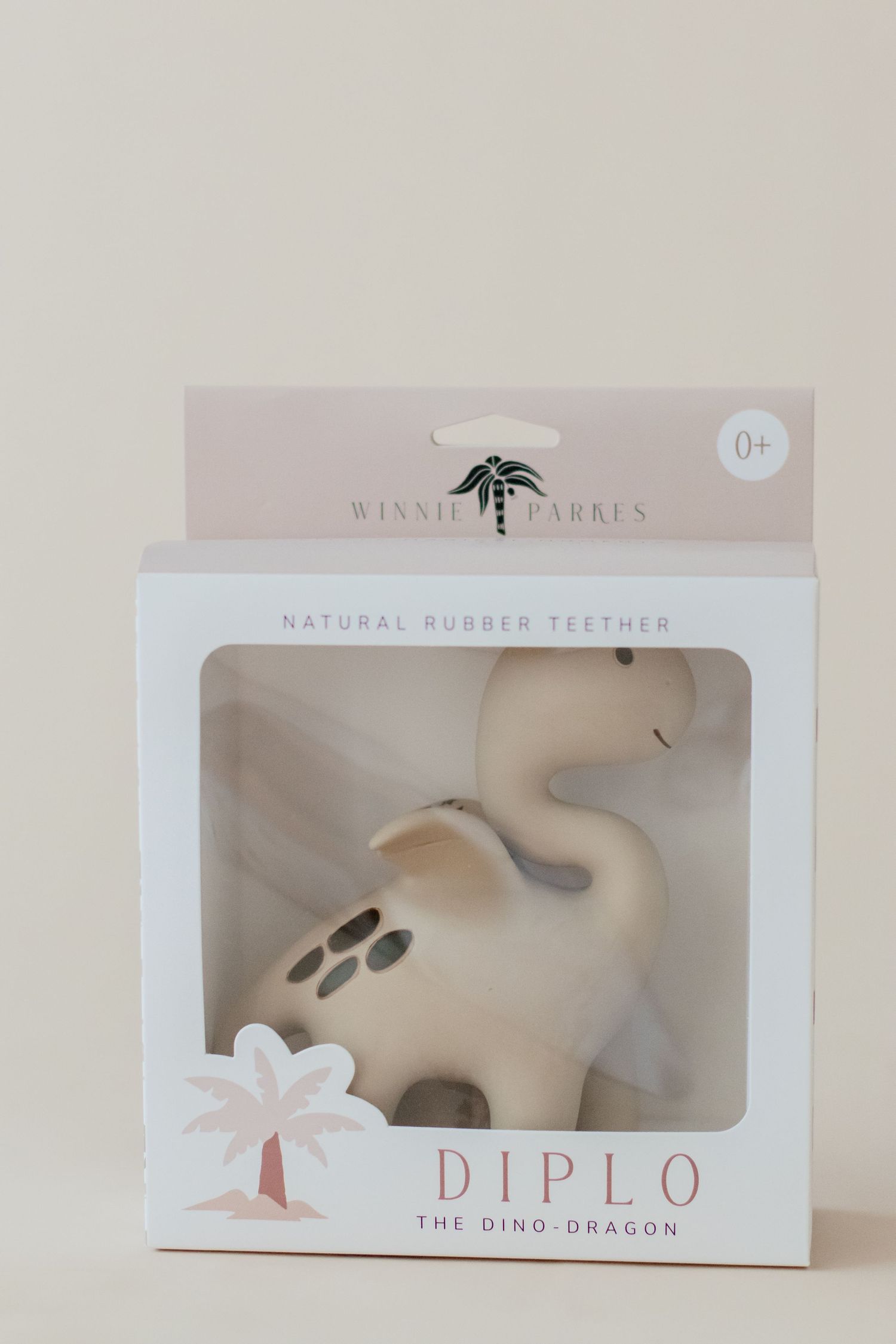 Natural rubber dinosaur teether toy in retail packaging against neutral background.