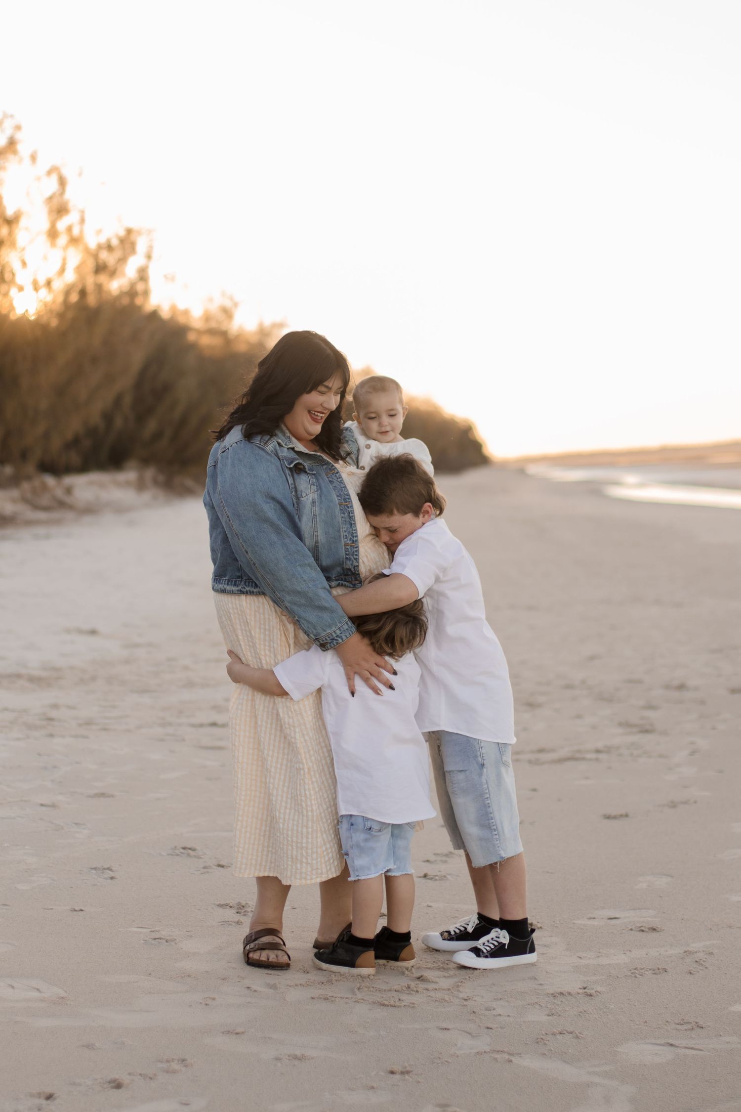 A touching family moment on the beach at sunset with gentle embraces and casual outfits on the sand.