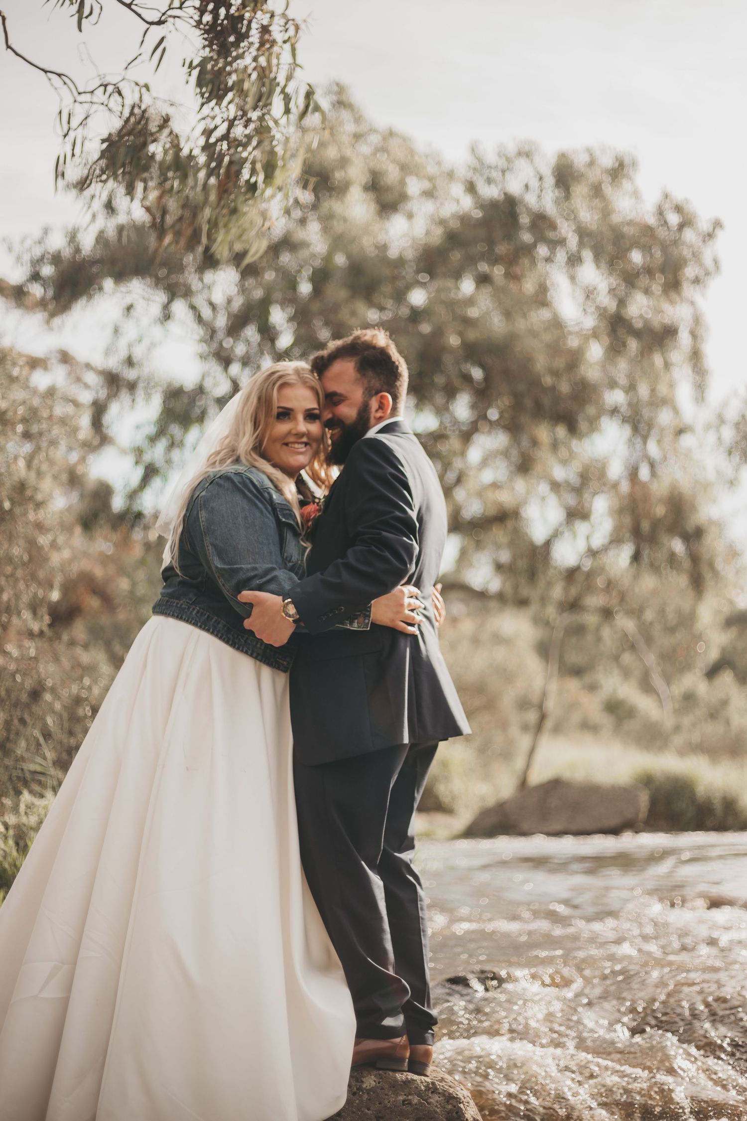 Couple sharing an intimate embrace outdoors during rustic wedding photoshoot with eucalyptus trees in background.