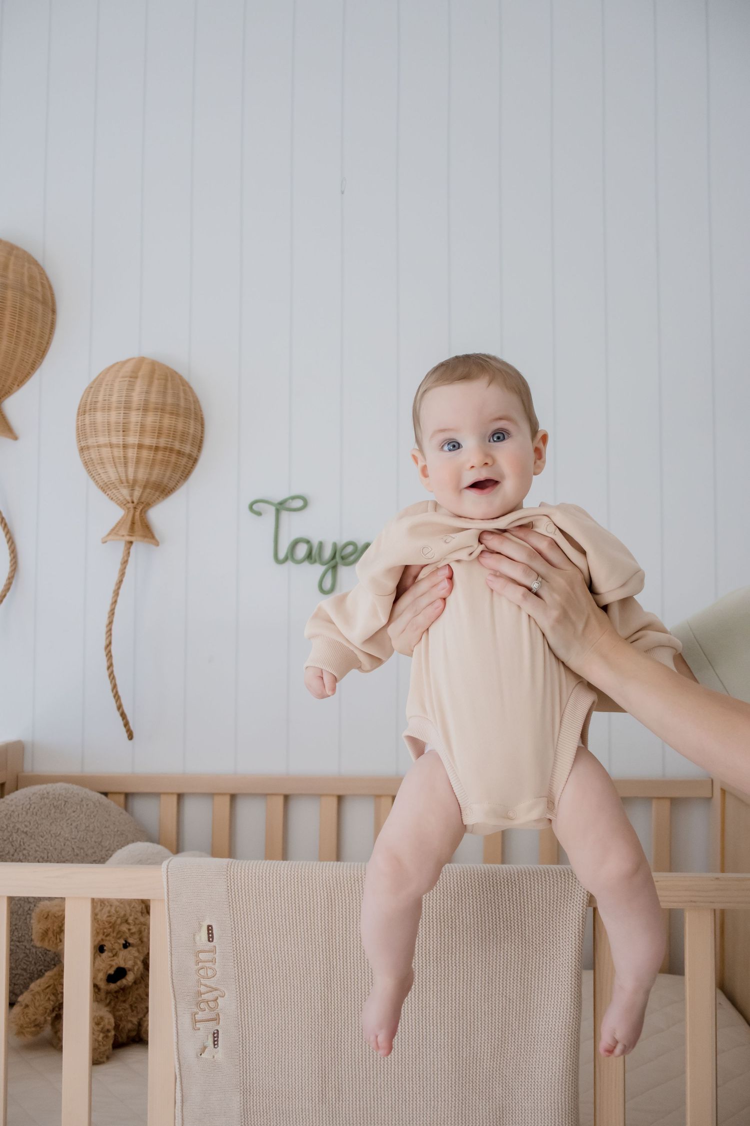 Baby in light peach outfit on crib with balloon wall decorations.