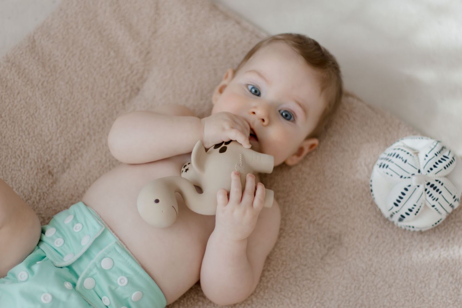 Baby lying on beige blanket with mint green cloth diaper.