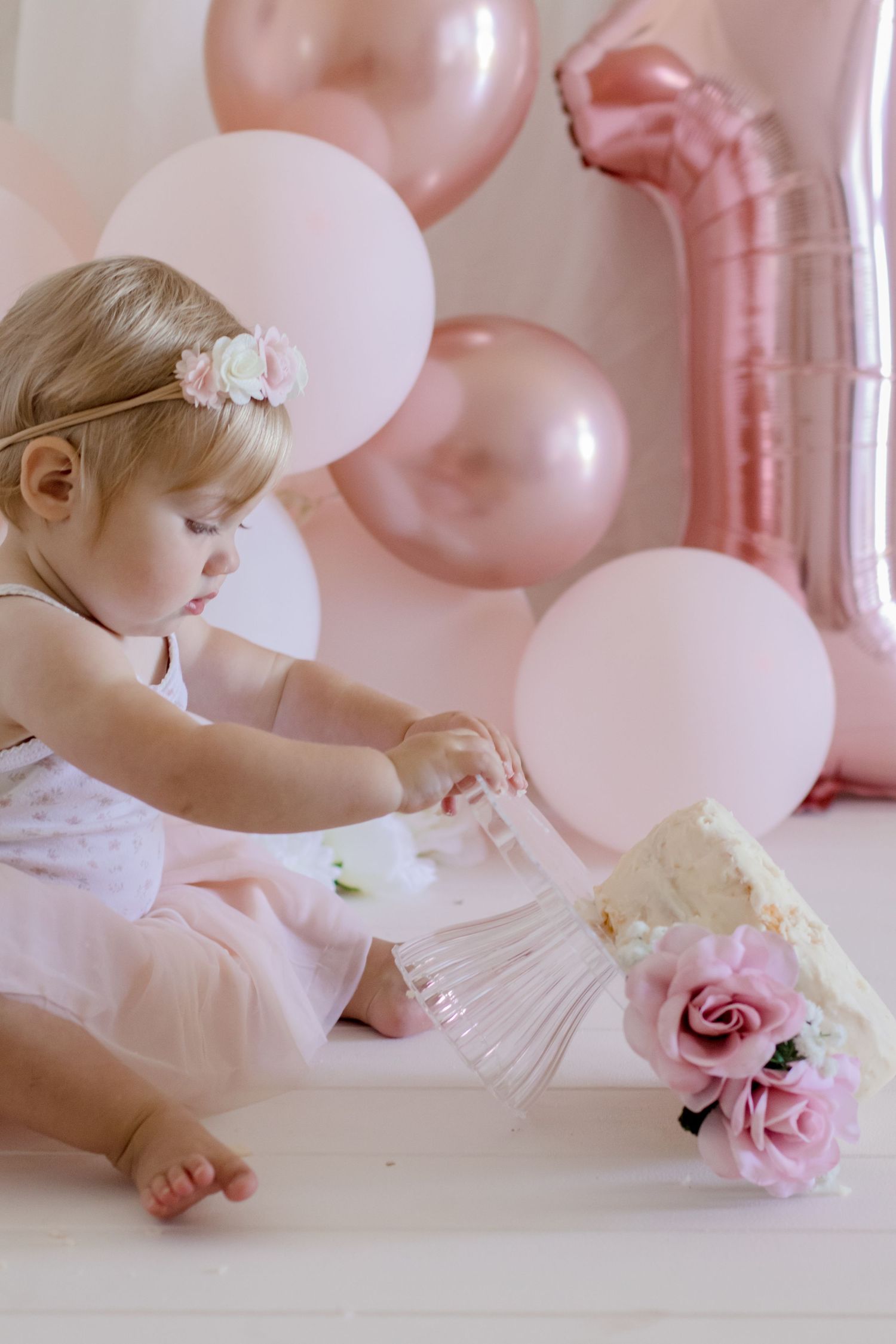 A gentle moment during a first birthday cake smash with pink roses and balloons.