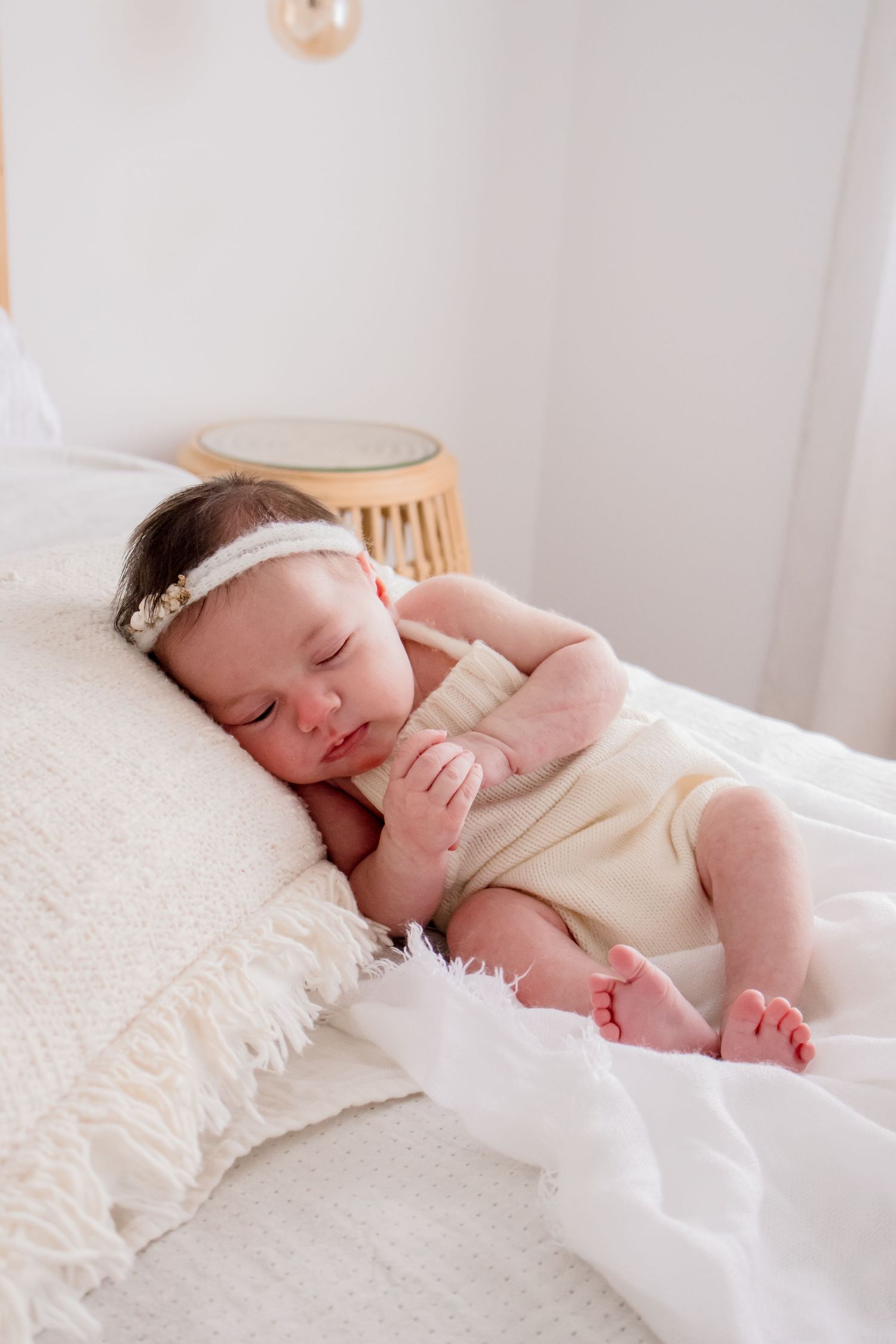 Sleeping infant in cream outfit on white textured bedding.