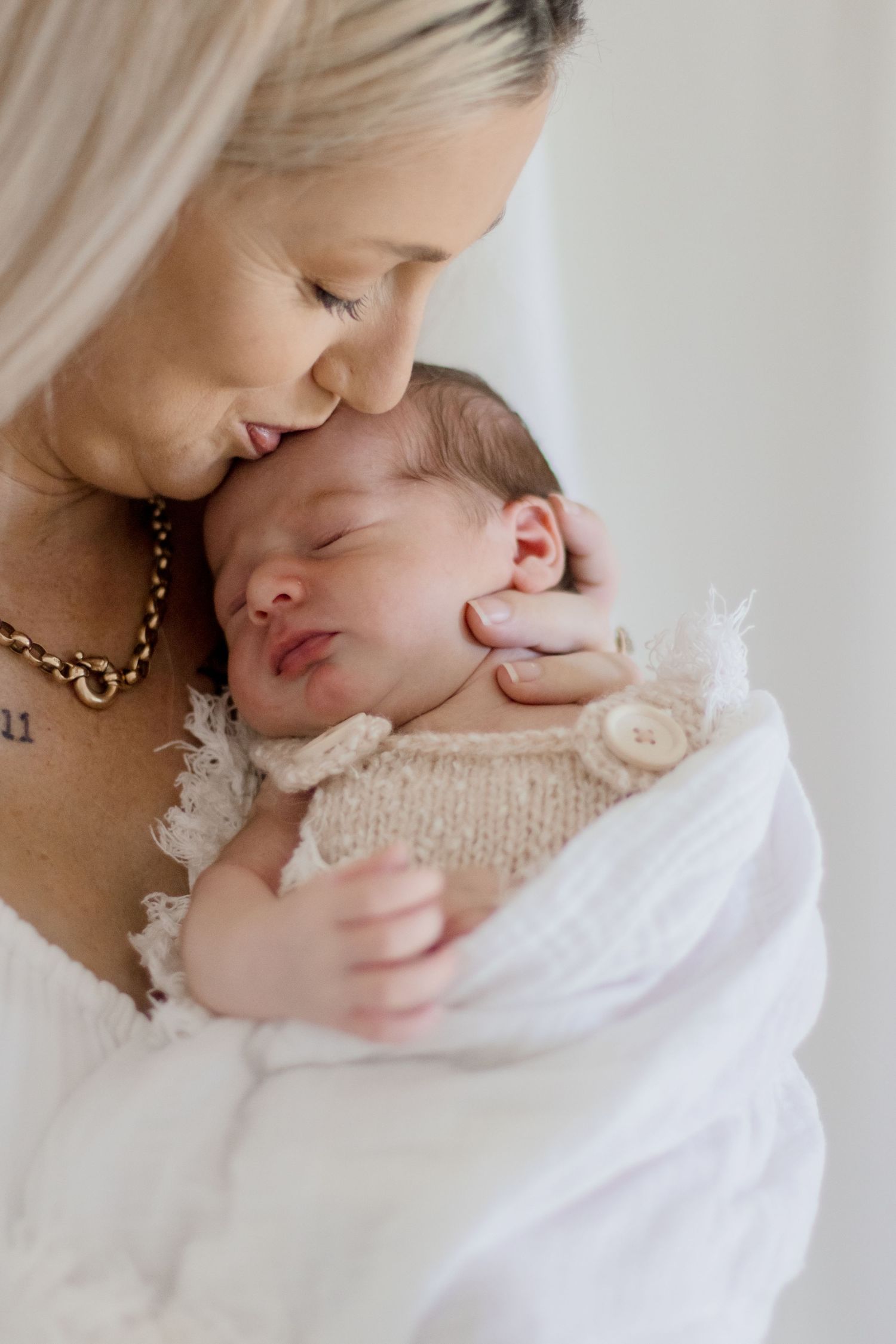 Intimate moment between mother and sleeping newborn baby in white attire.