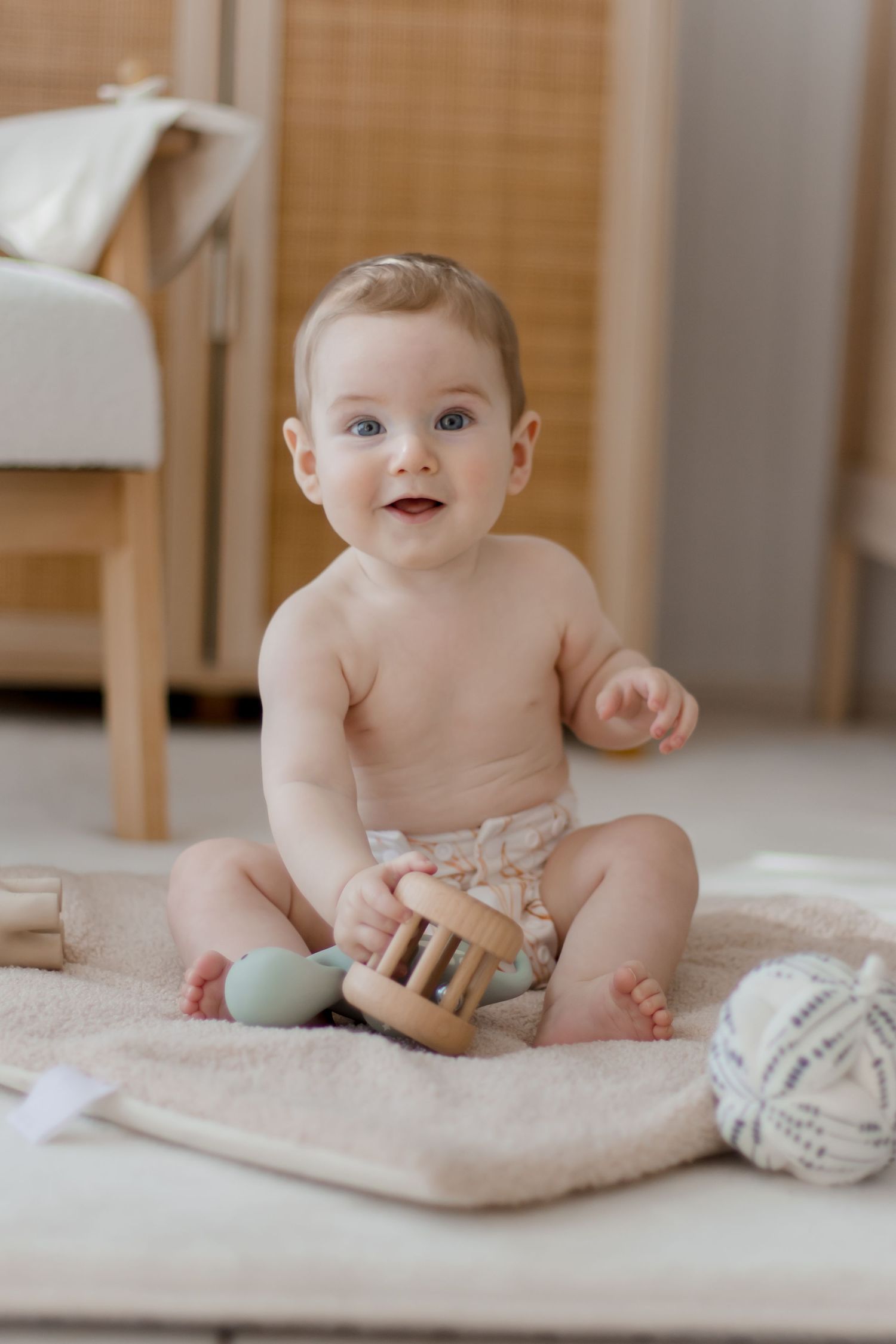 Baby sitting on plush carpet playing with wooden toys in natural light setting.