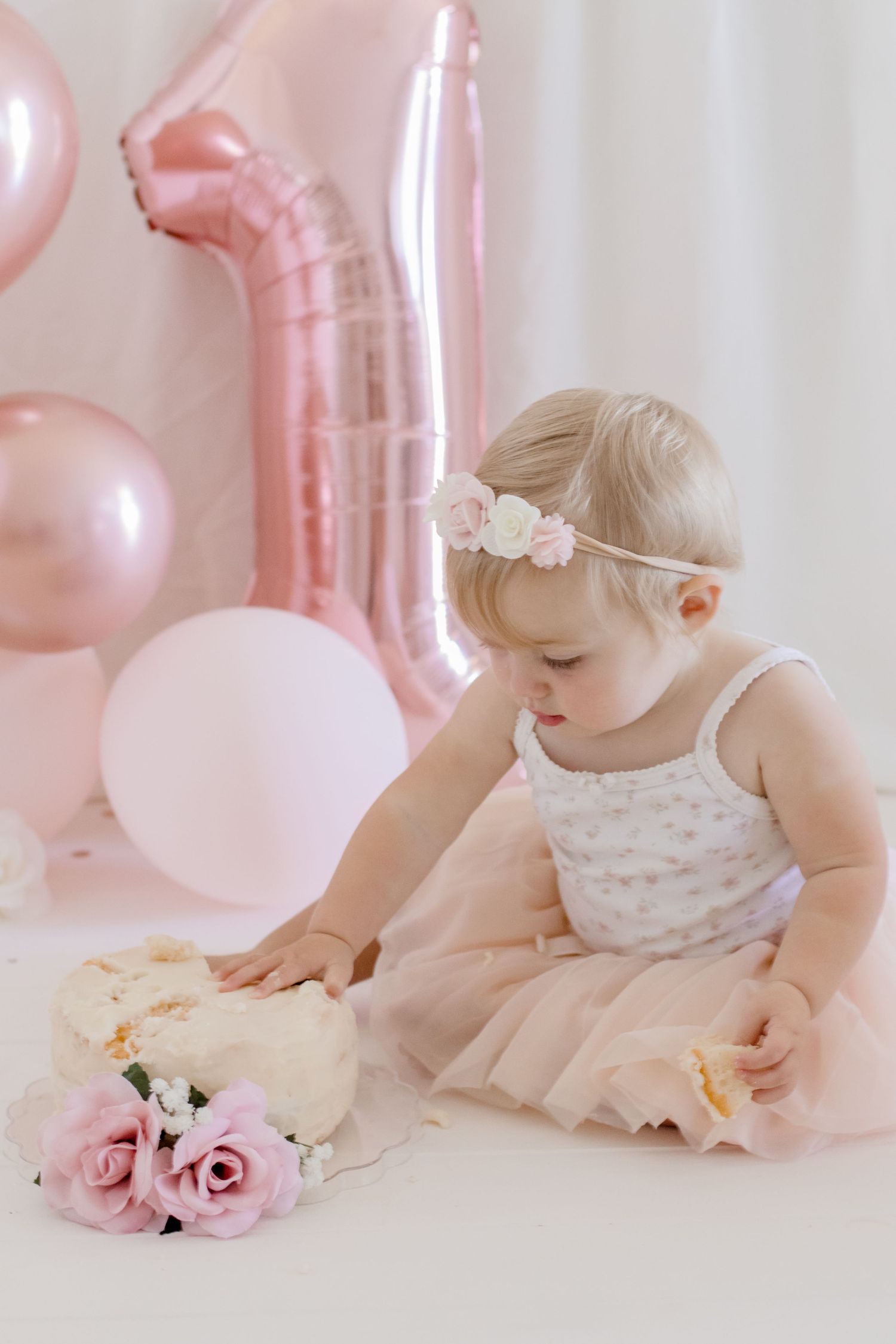Baby in tulle dress looking down at pink roses with balloon decorations.