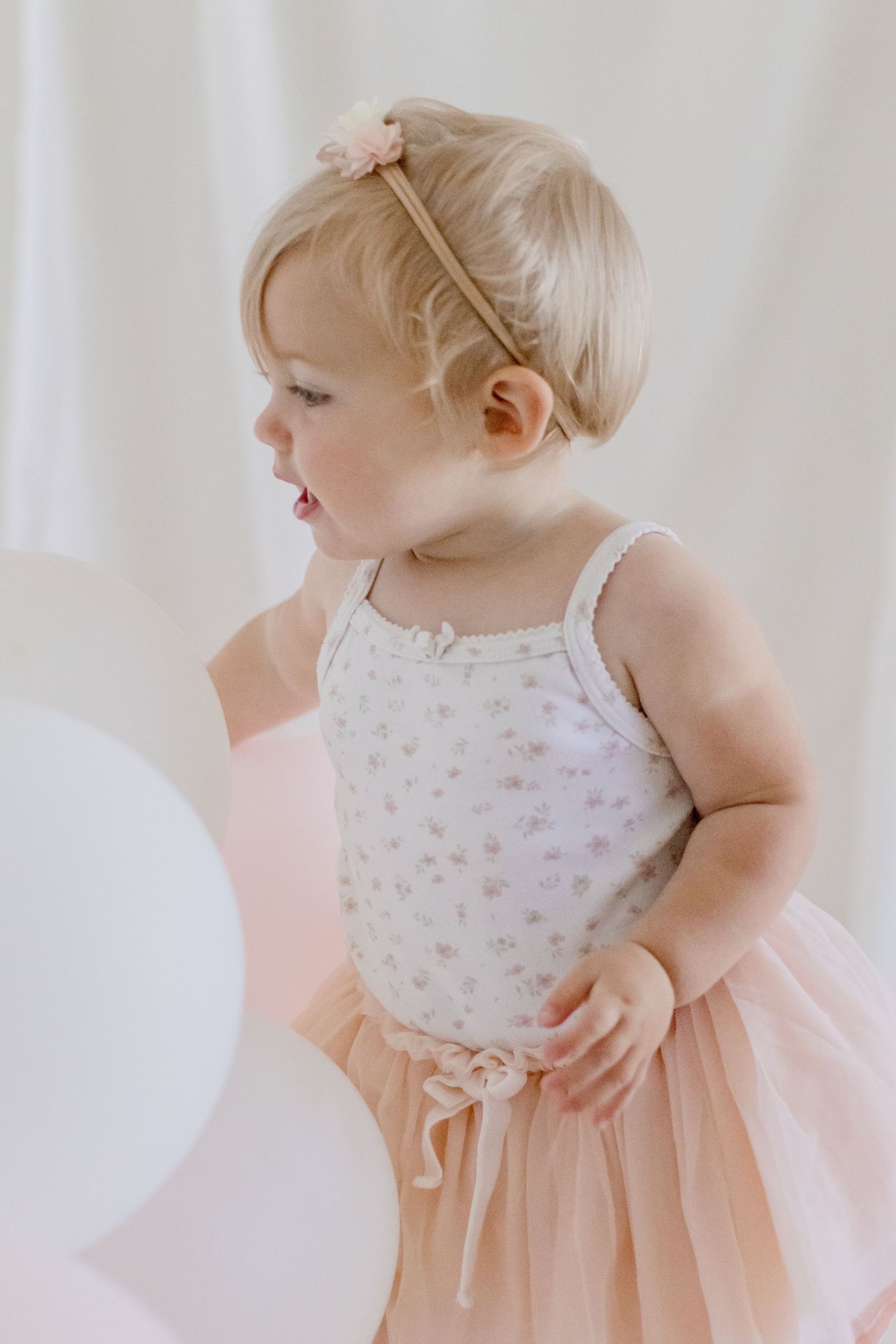 Toddler wearing pink tulle dress and delicate headband in soft portrait setting.