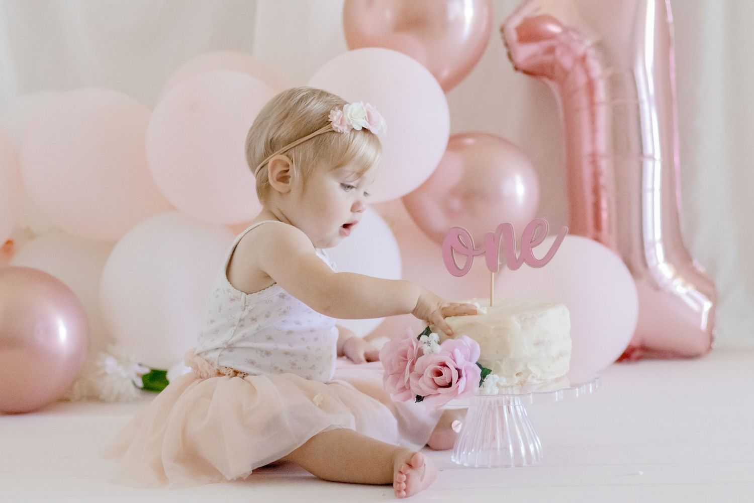 First birthday photoshoot featuring cake, pink balloons, and delicate floral decorations.