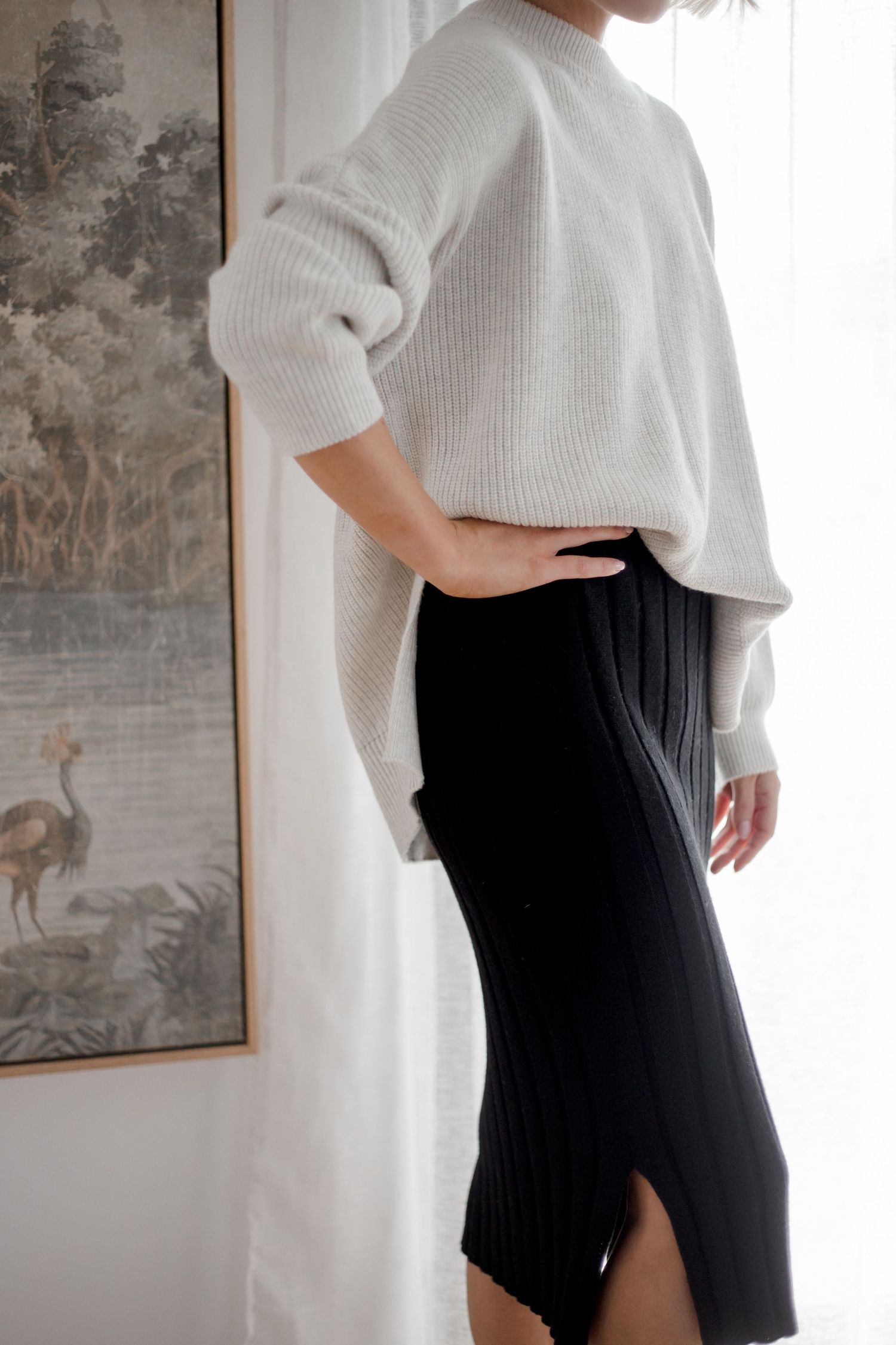 Minimalist winter outfit featuring a cozy white knit sweater paired with a black ribbed midi skirt against a light interior.