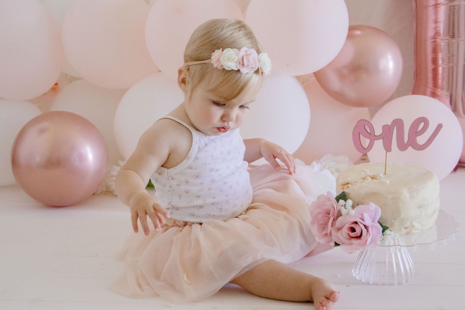 First birthday setup with baby in tutu dress surrounded by pink balloons and roses.