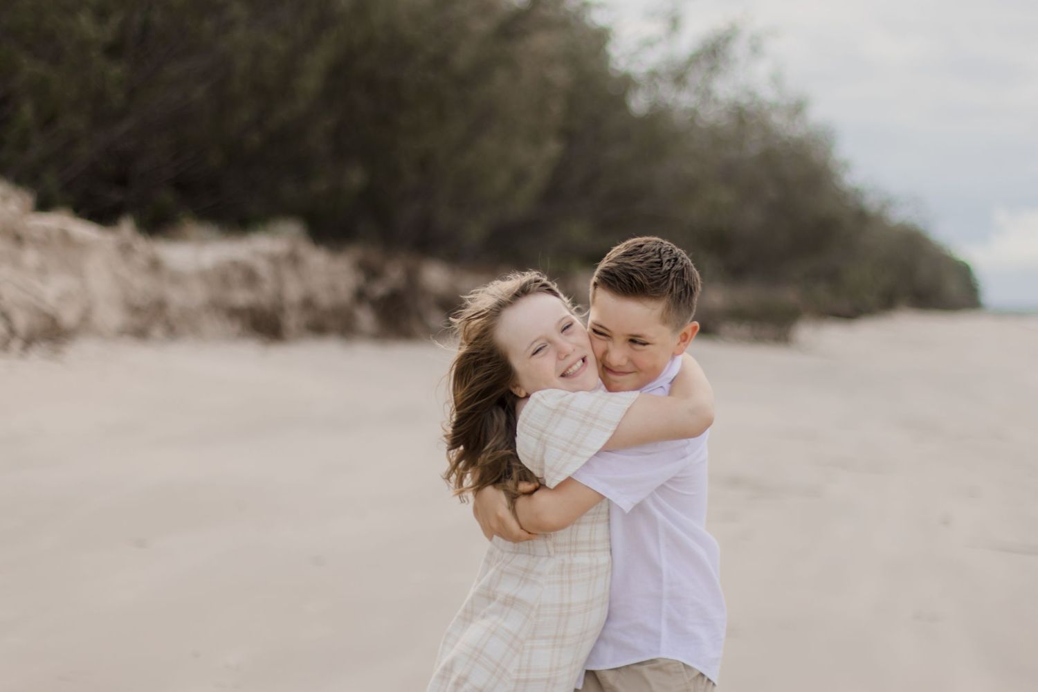 Two people sharing a joyful embrace while laughing on a sandy beach.