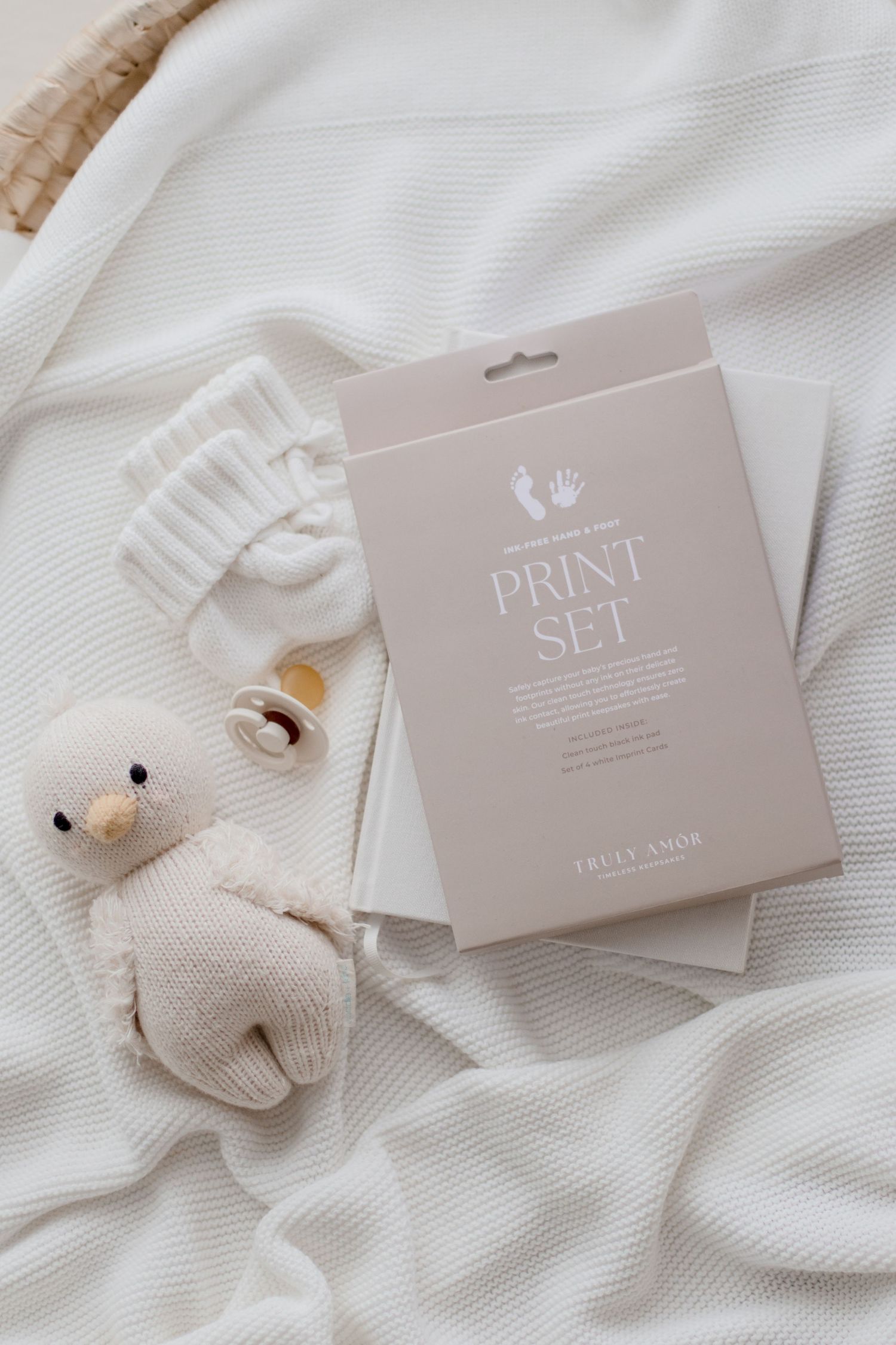 White knit baby accessories and gift packaging cards arranged on a textured white fabric background.