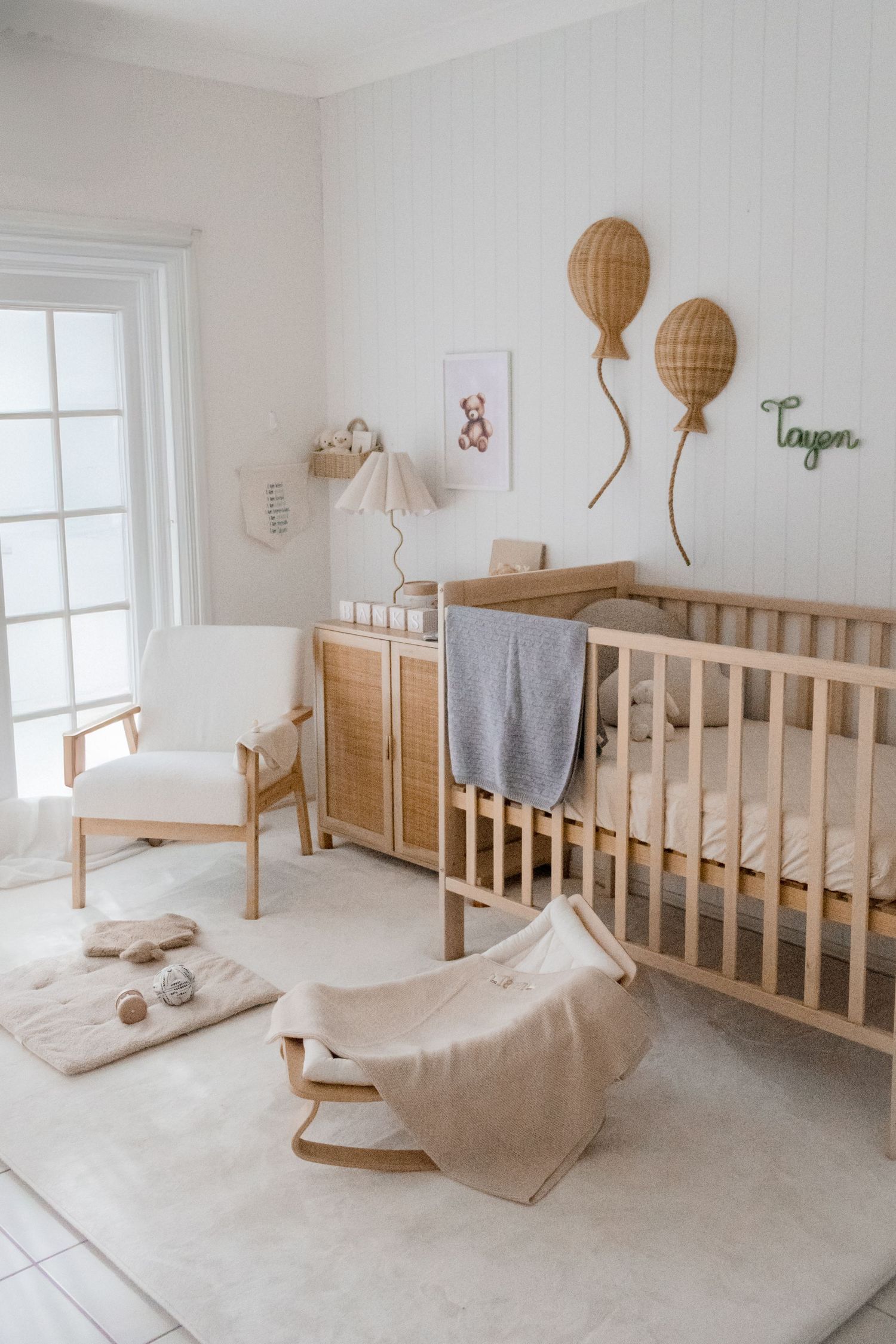 Minimalist nursery with wooden cribs, woven balloon wall decor, and neutral color scheme.