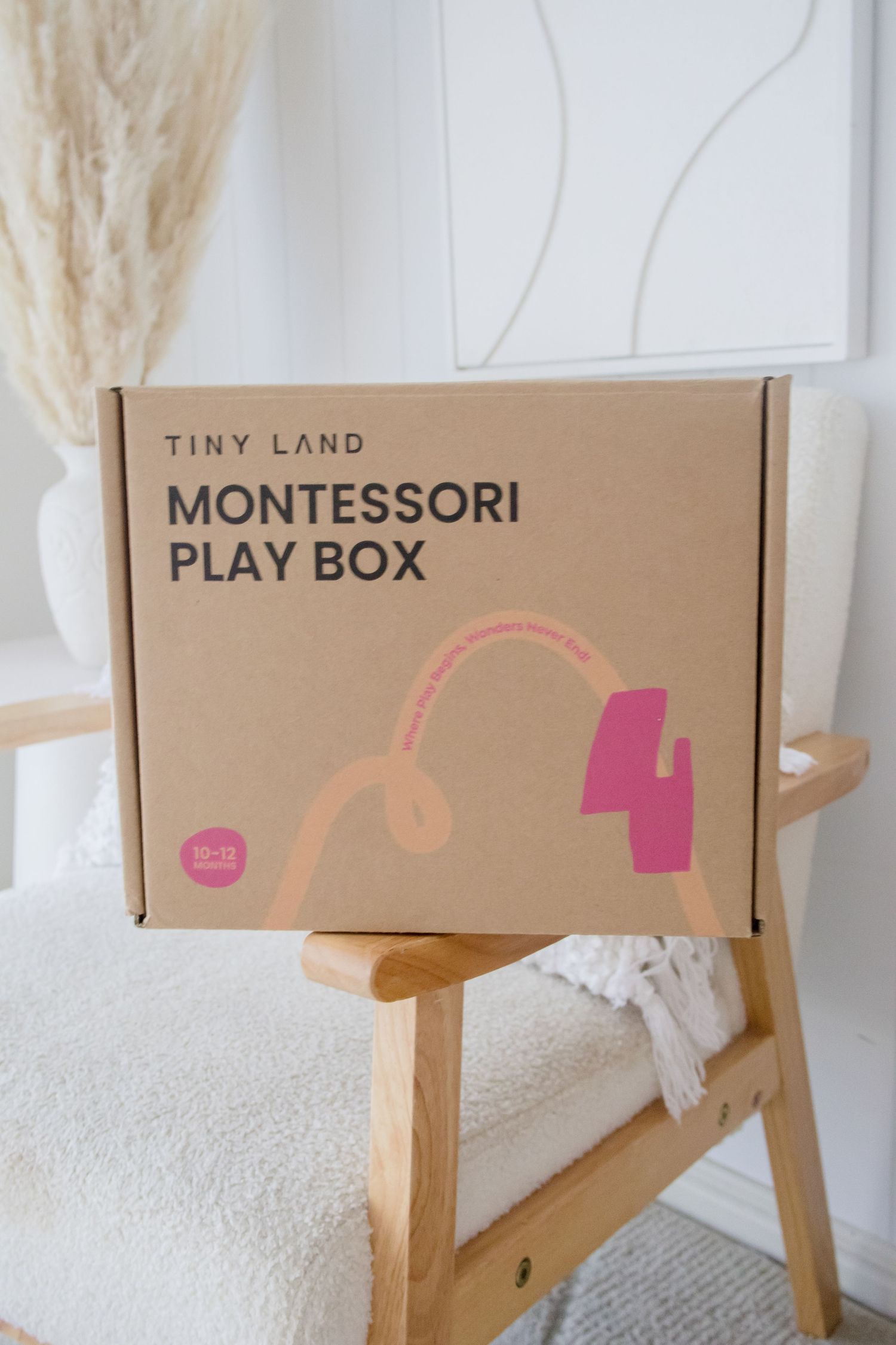 Tiny Land Montessori Play Box package displayed on wooden chair with white decor.