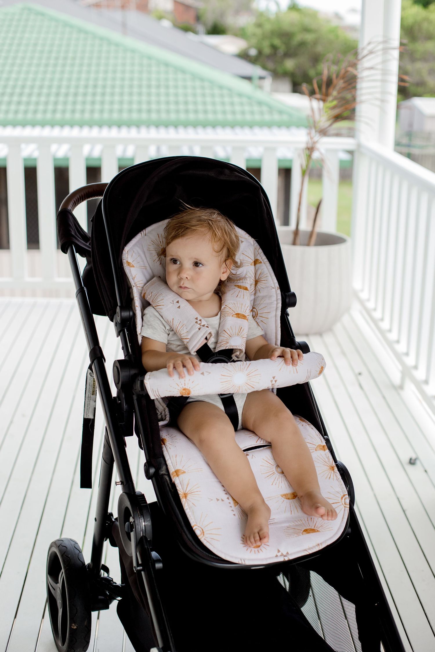 Child sitting in black and white stroller on white porch with green roof in background.