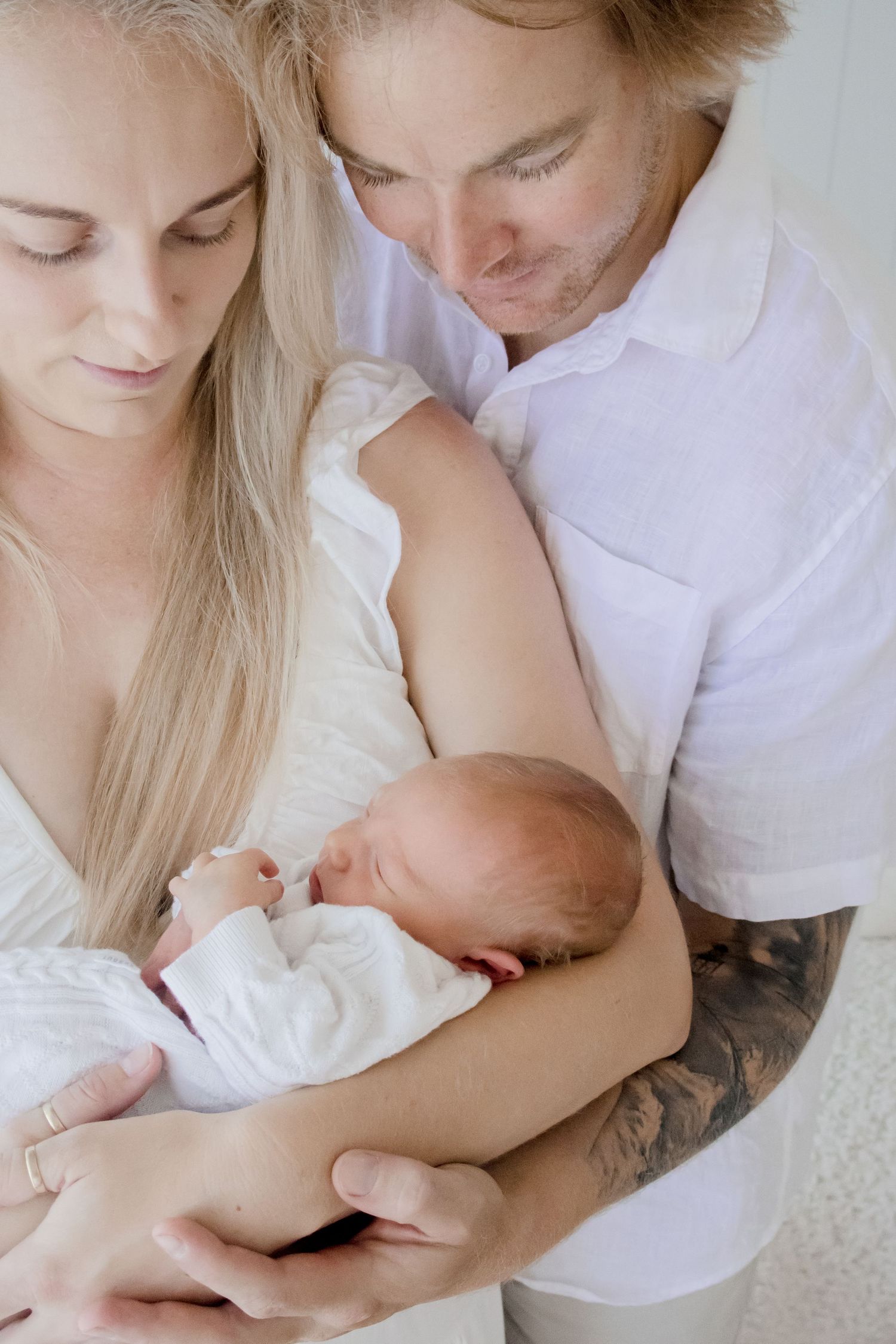 Intimate family moment as couple cuddles their newborn baby while wearing white.