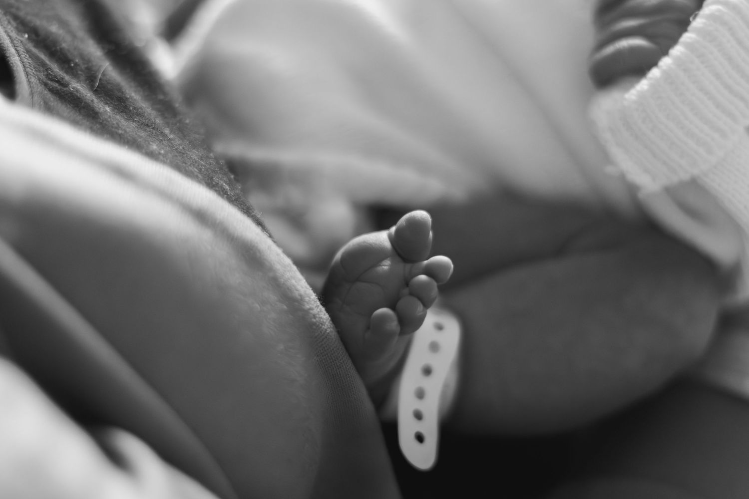 Black and white close-up of newborn baby feet with hospital identification tag.