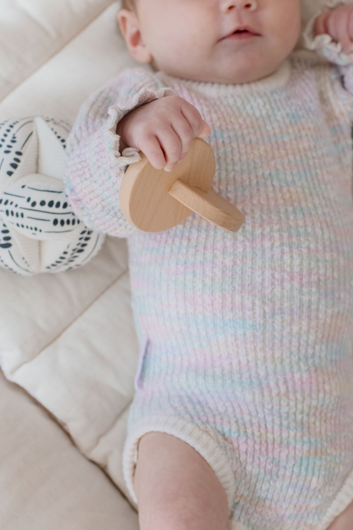 Close up view of baby in striped pastel knitwear on cream colored bedding.