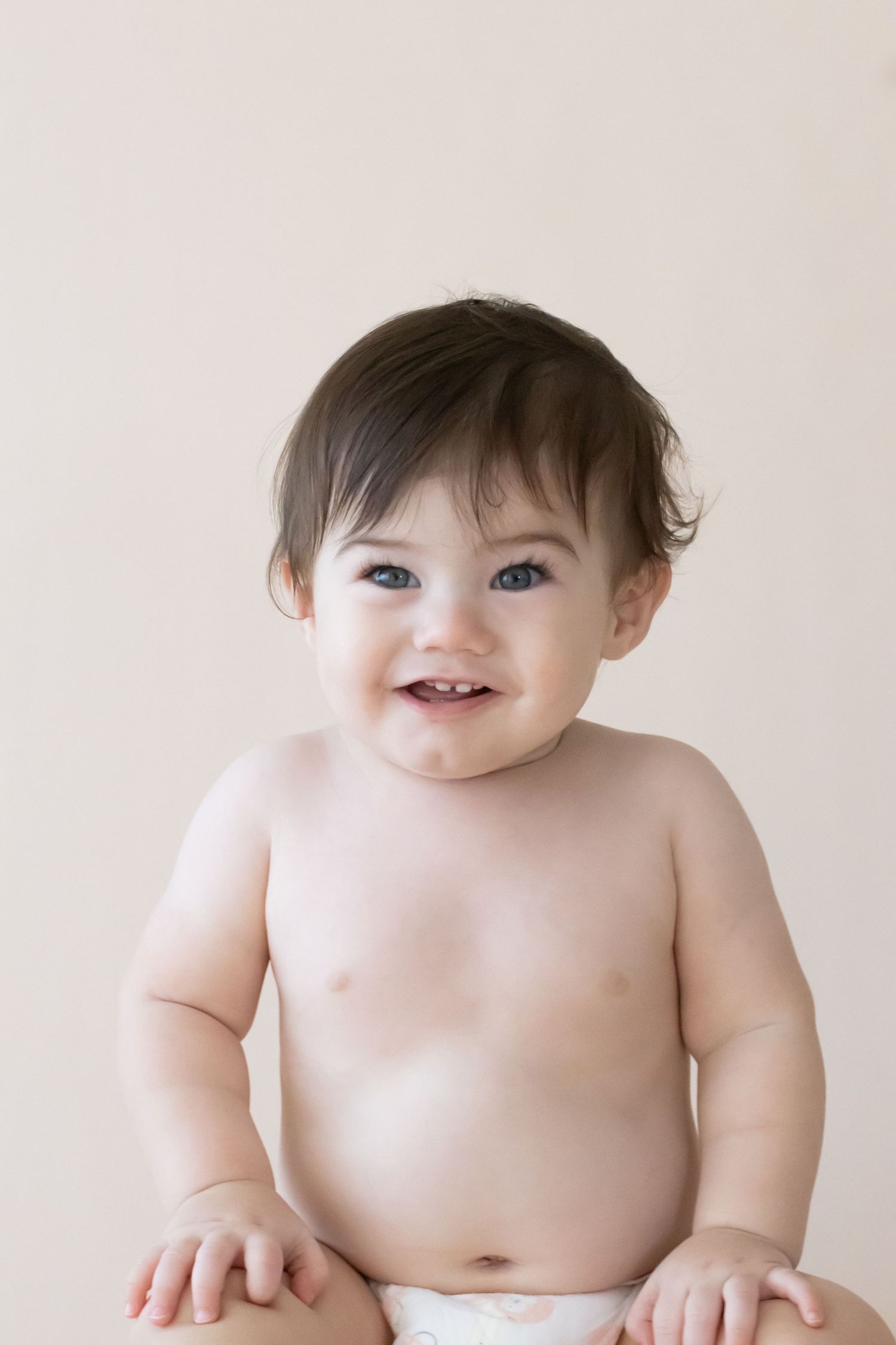 Smiling baby wearing only a diaper sits against neutral background.