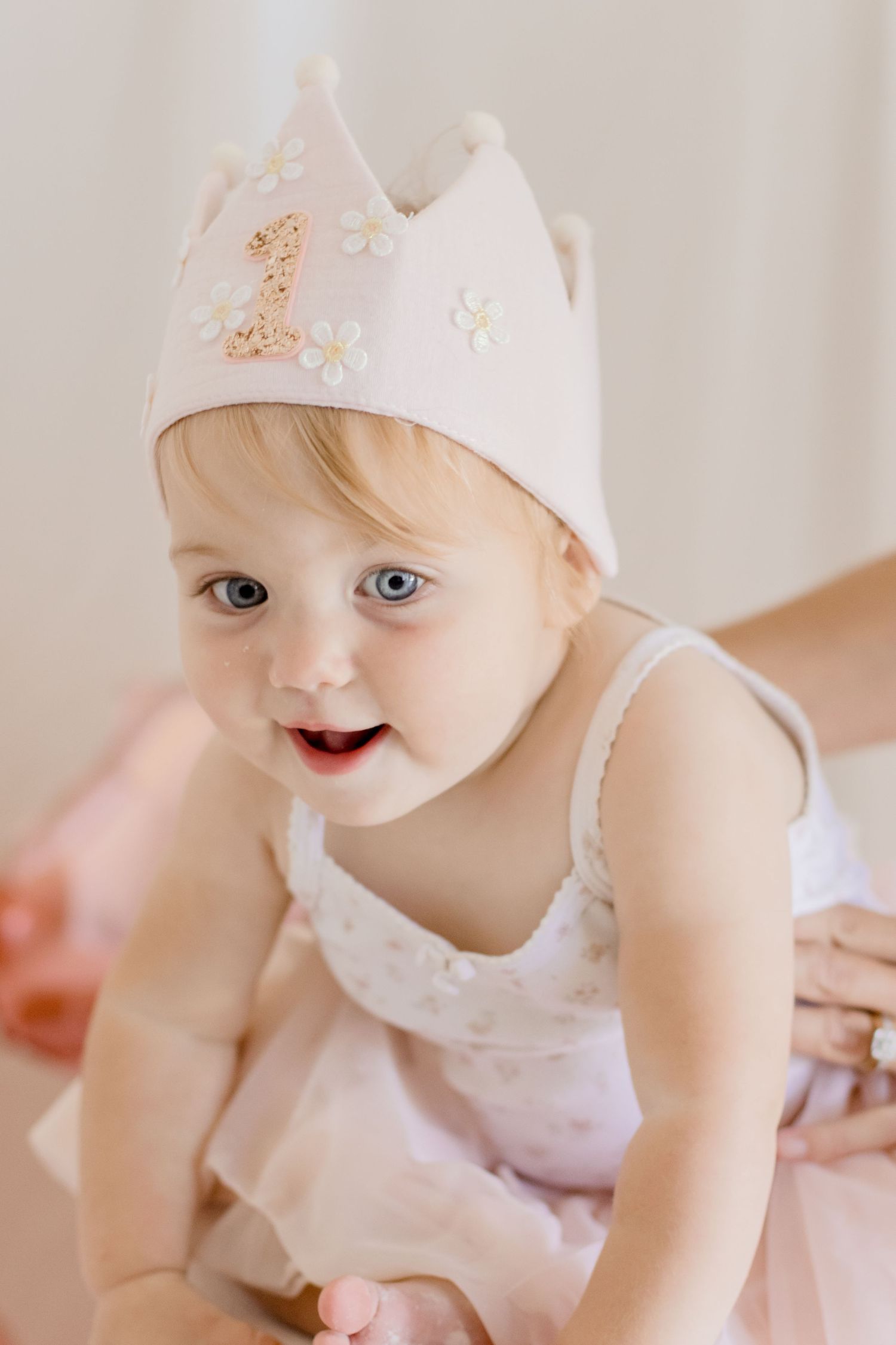 A happy baby wearing a pink tutu and crown smiles brightly against a light background.