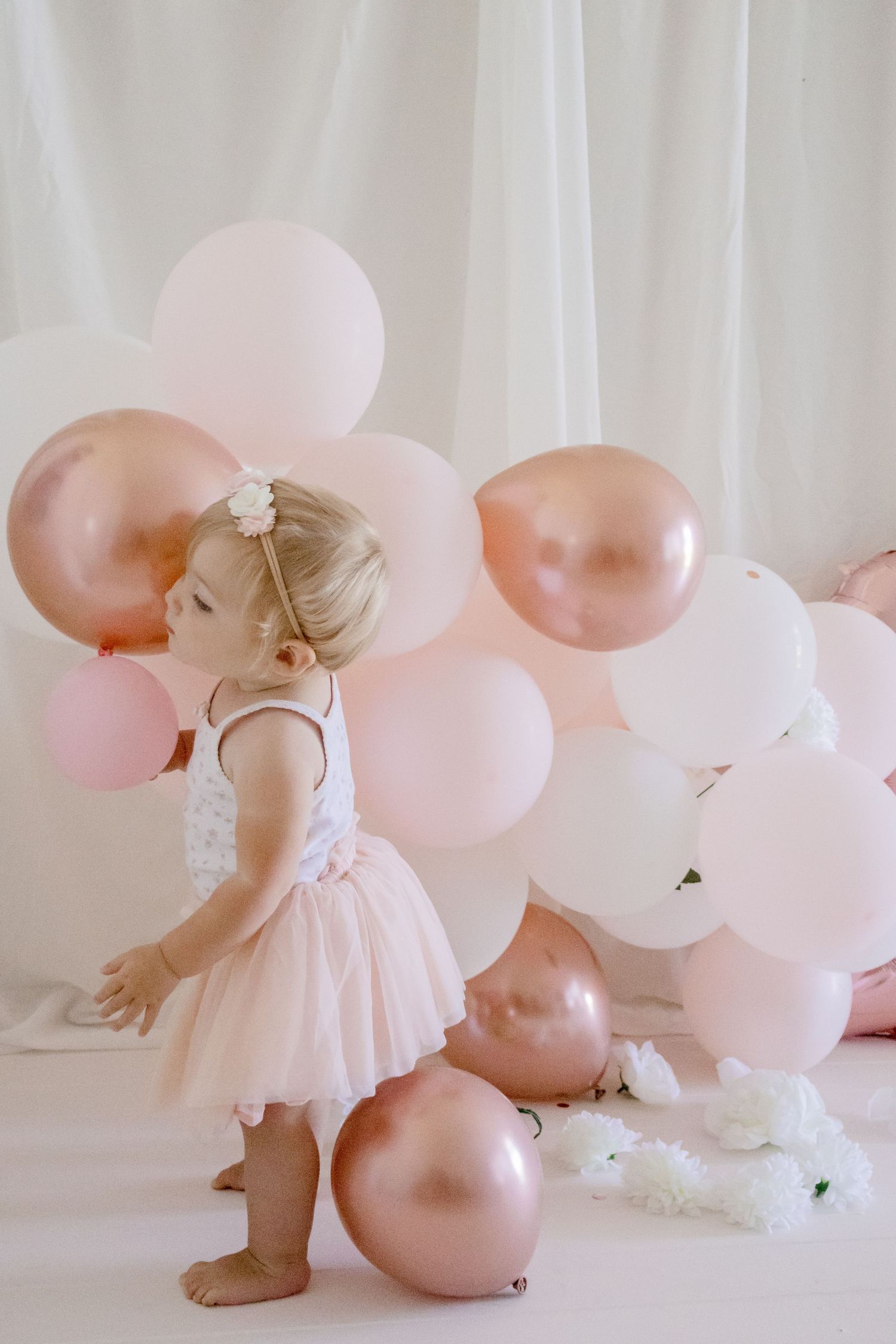 Toddler in ballet-inspired outfit playing among pink and rose gold balloons.