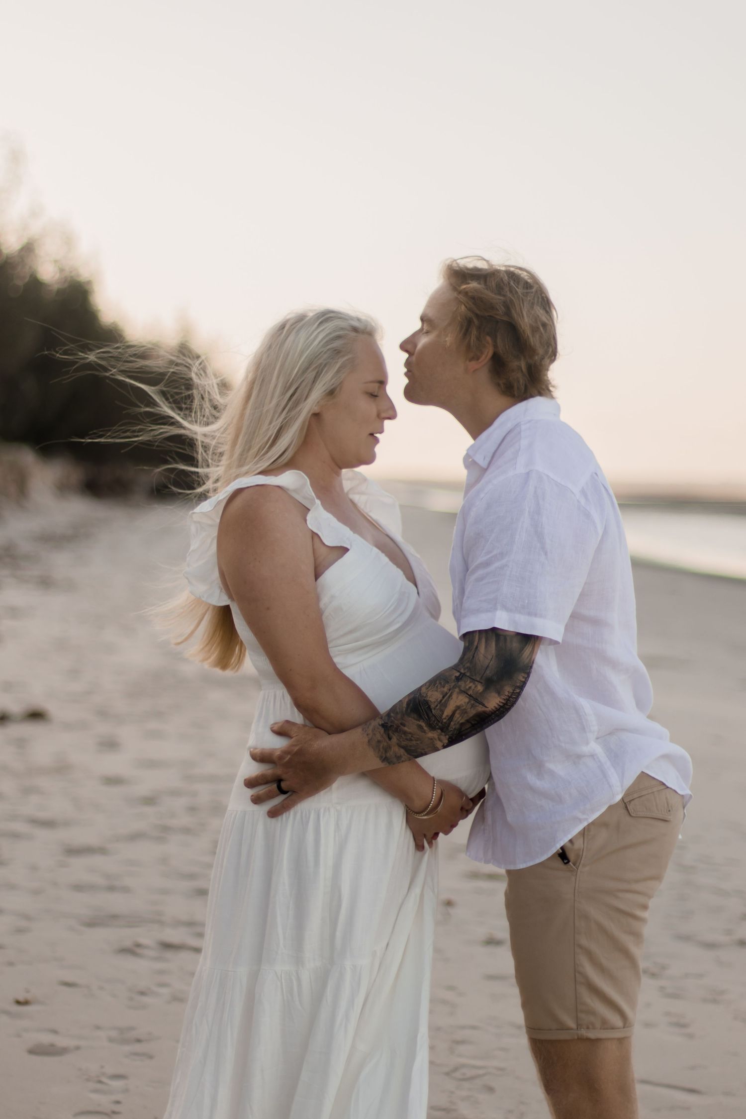 Couple in white sharing an intimate moment on a beach at sunset.