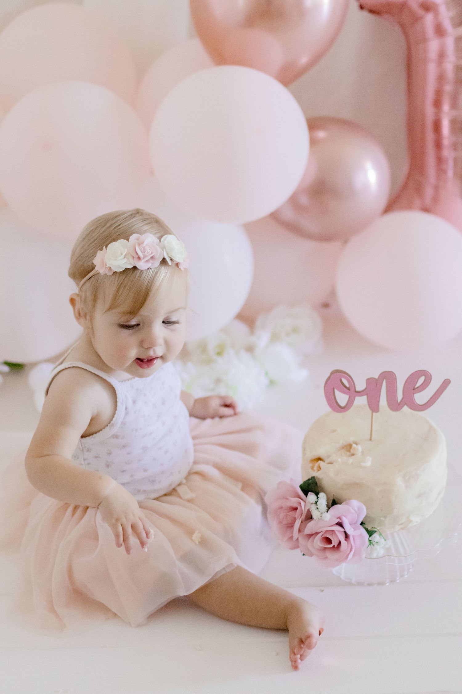 Pink and white themed first birthday setup with tulle dress and decorated cake.