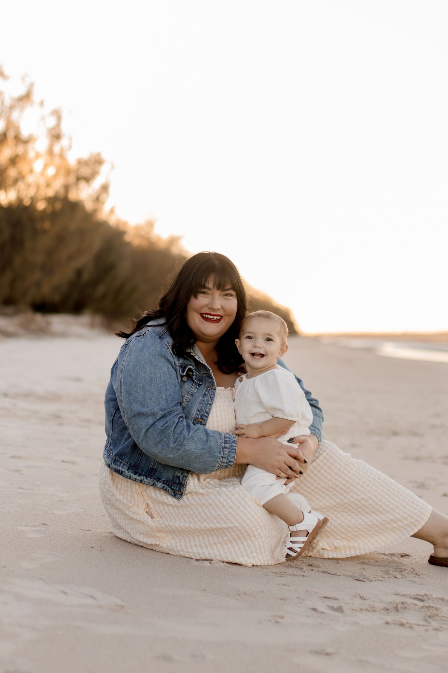 Two people sharing joyful moments while sitting together on a sandy beach at sunset.
