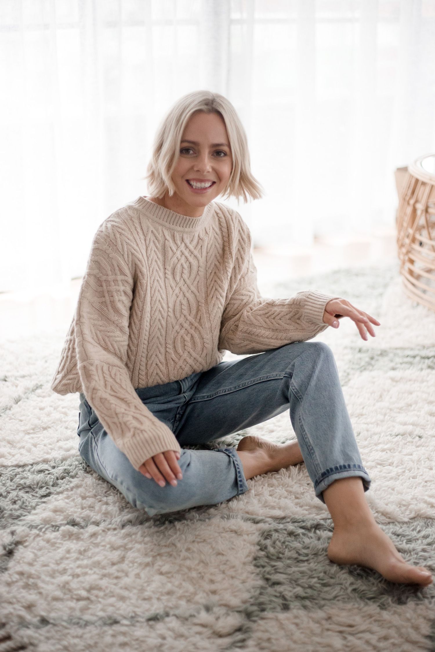 Casual autumn outfit featuring beige cable knit sweater and relaxed fit jeans on cozy white carpet.