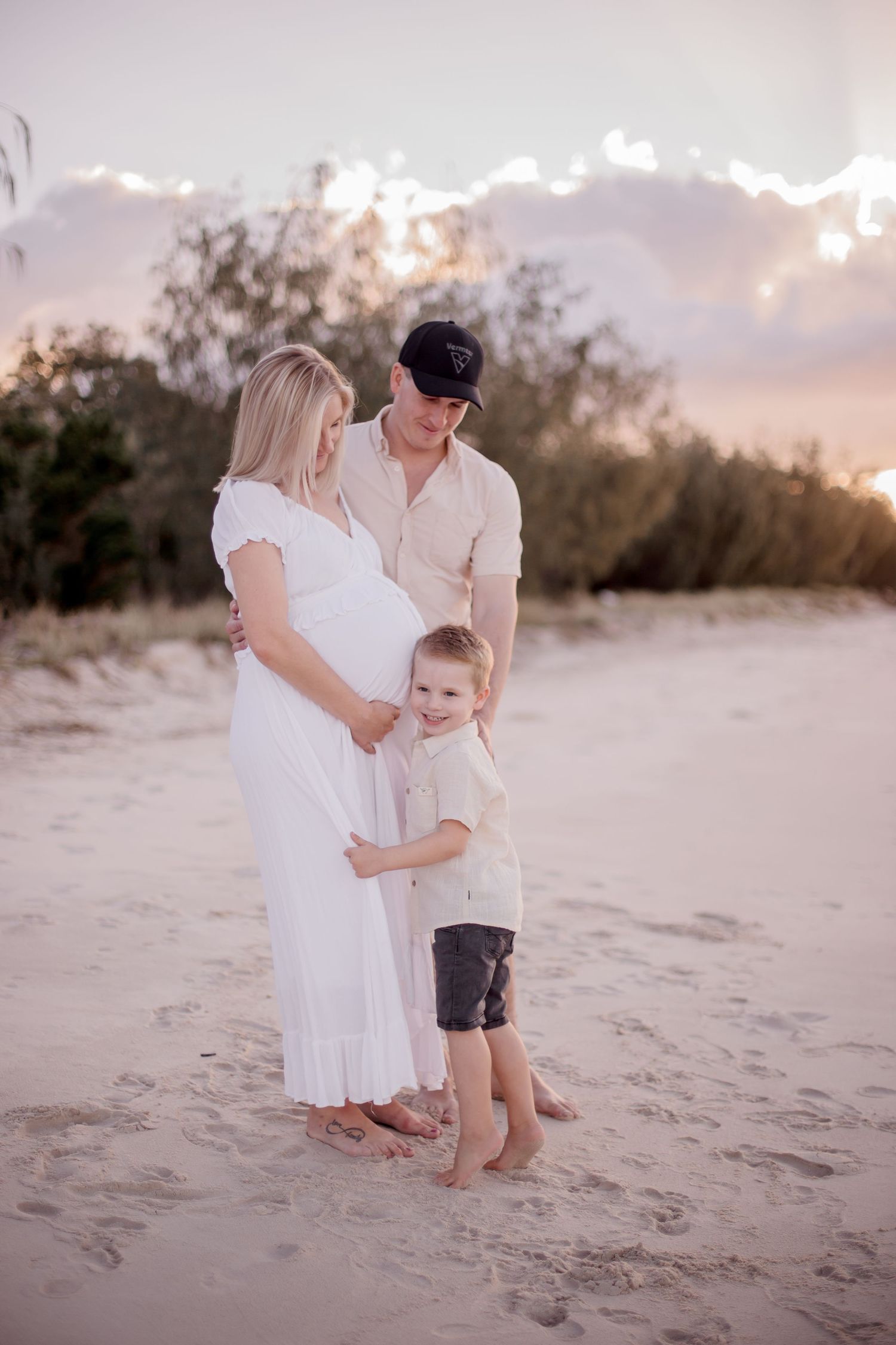 A heartwarming family maternity photo session on a sandy beach during golden hour sunset.