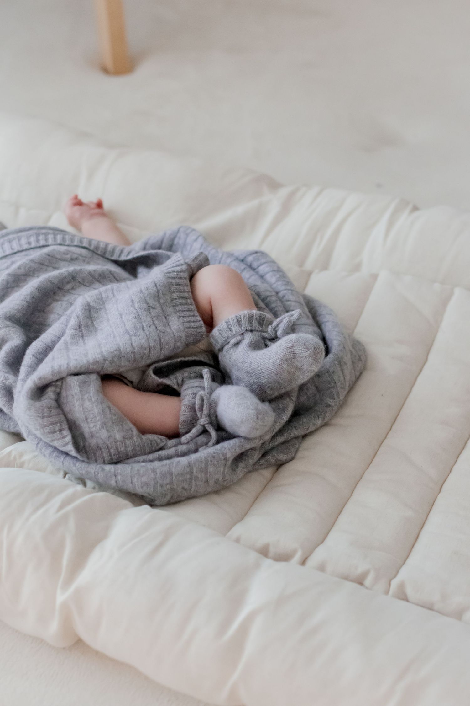 Infant wrapped in soft gray knit blanket lying on quilted white mat.