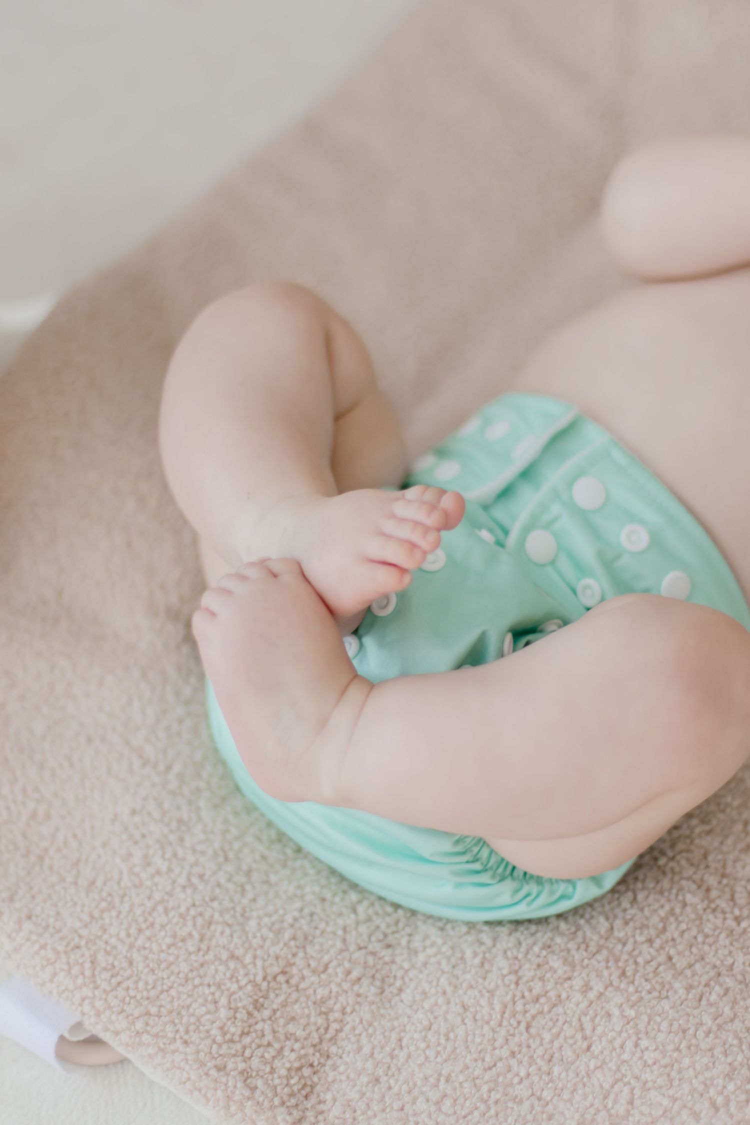 Close-up of baby legs wearing mint green cloth diaper against beige fabric.
